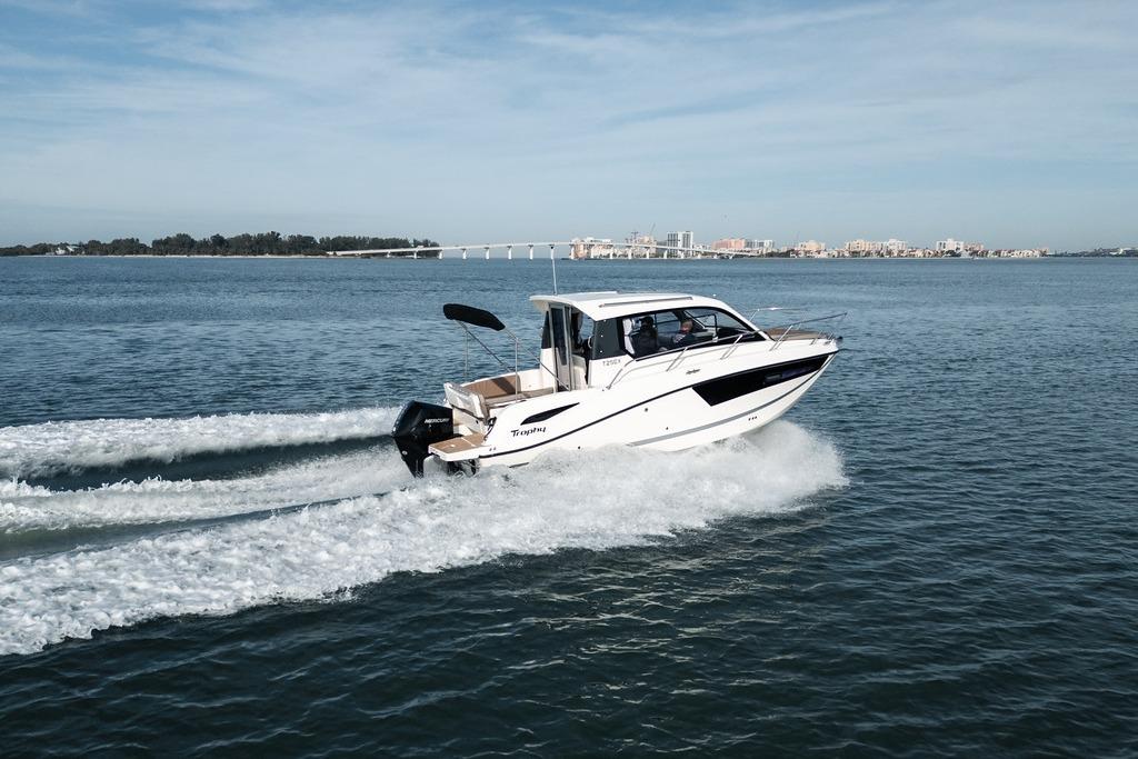 2026 Trophy T25EX Explorer OB boat cruising on open water, cityscape in background.