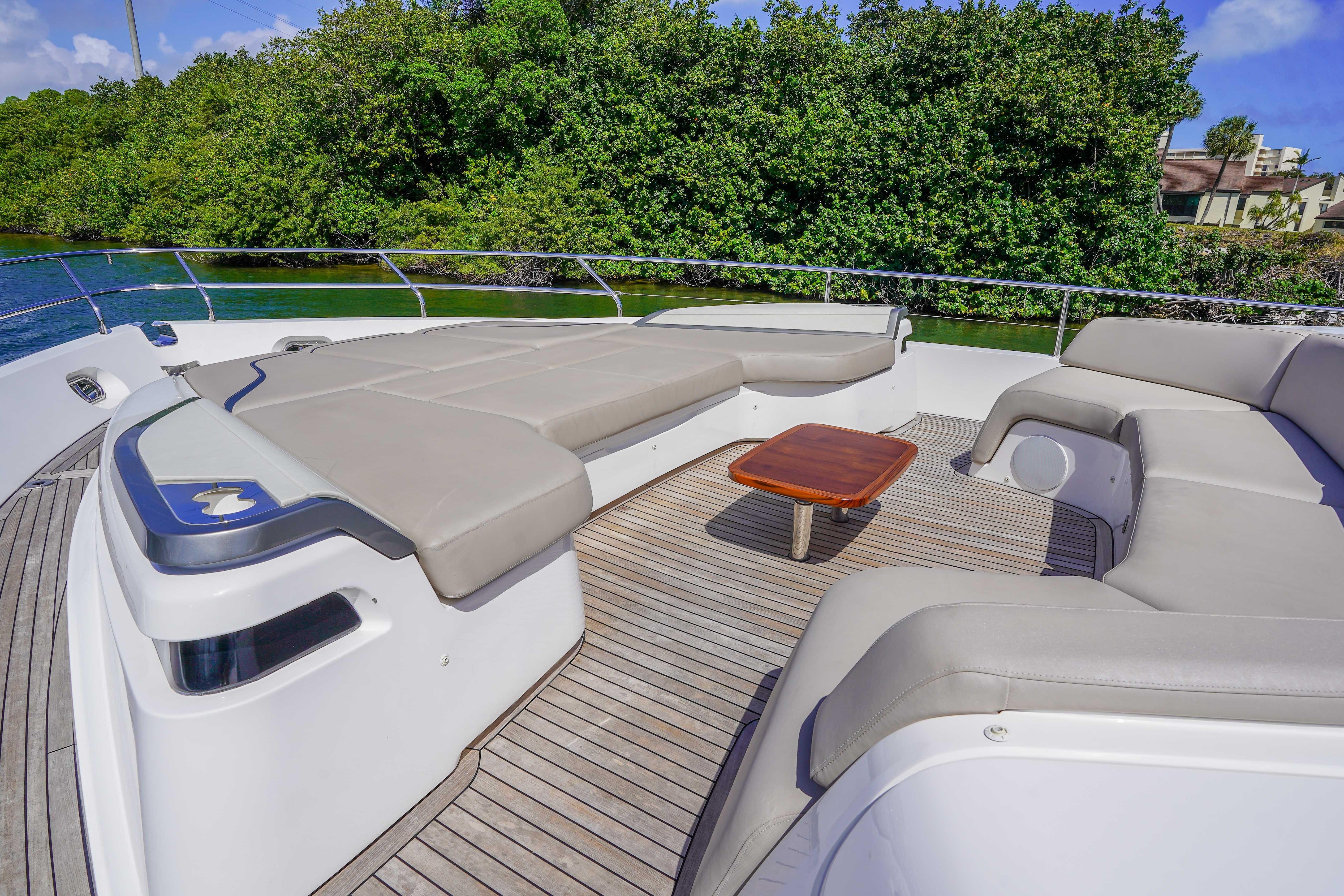 Luxurious 2021 Princess Y85 yacht deck with plush seating and wooden table, surrounded by lush greenery.