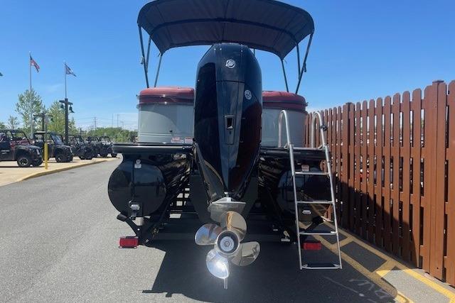 2026 Regency 250 DL pontoon boat with outboard motor and canopy, parked near a wooden fence.