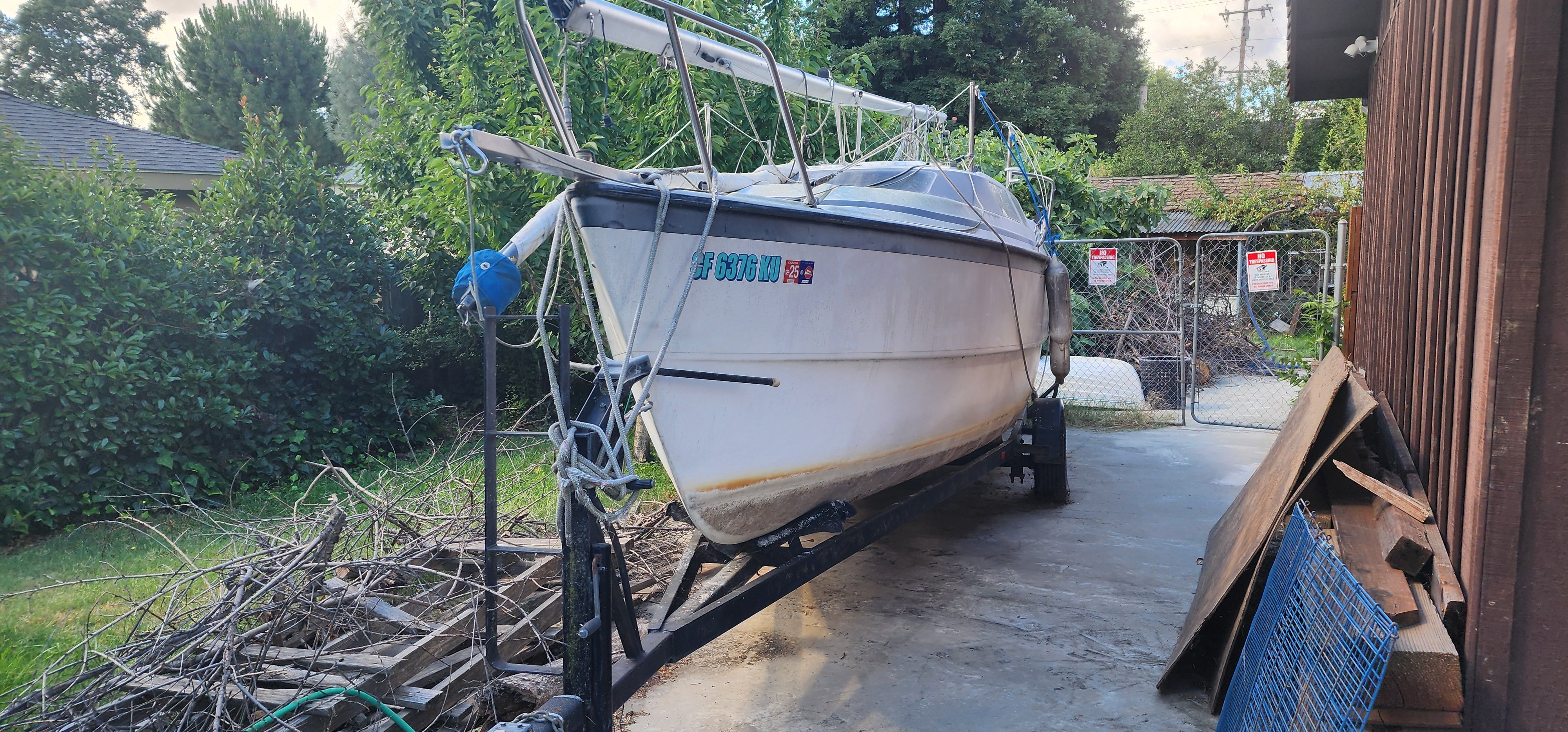 A 1995 MacGregor 26X sailboat on a trailer in a yard.