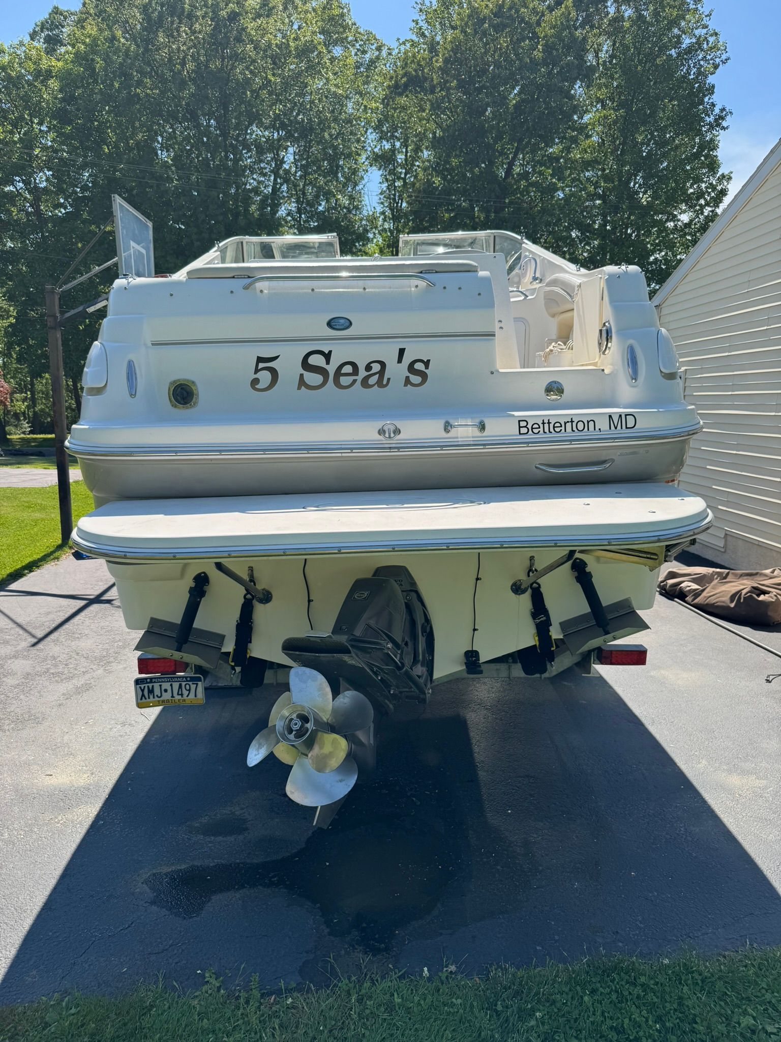 A white motorboat named "5 Sea's" is on a trailer in a yard.