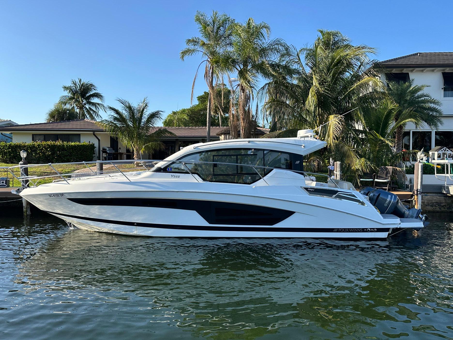 2020 Four Winns Vista 355 Coupe docked by palm trees and waterfront homes.