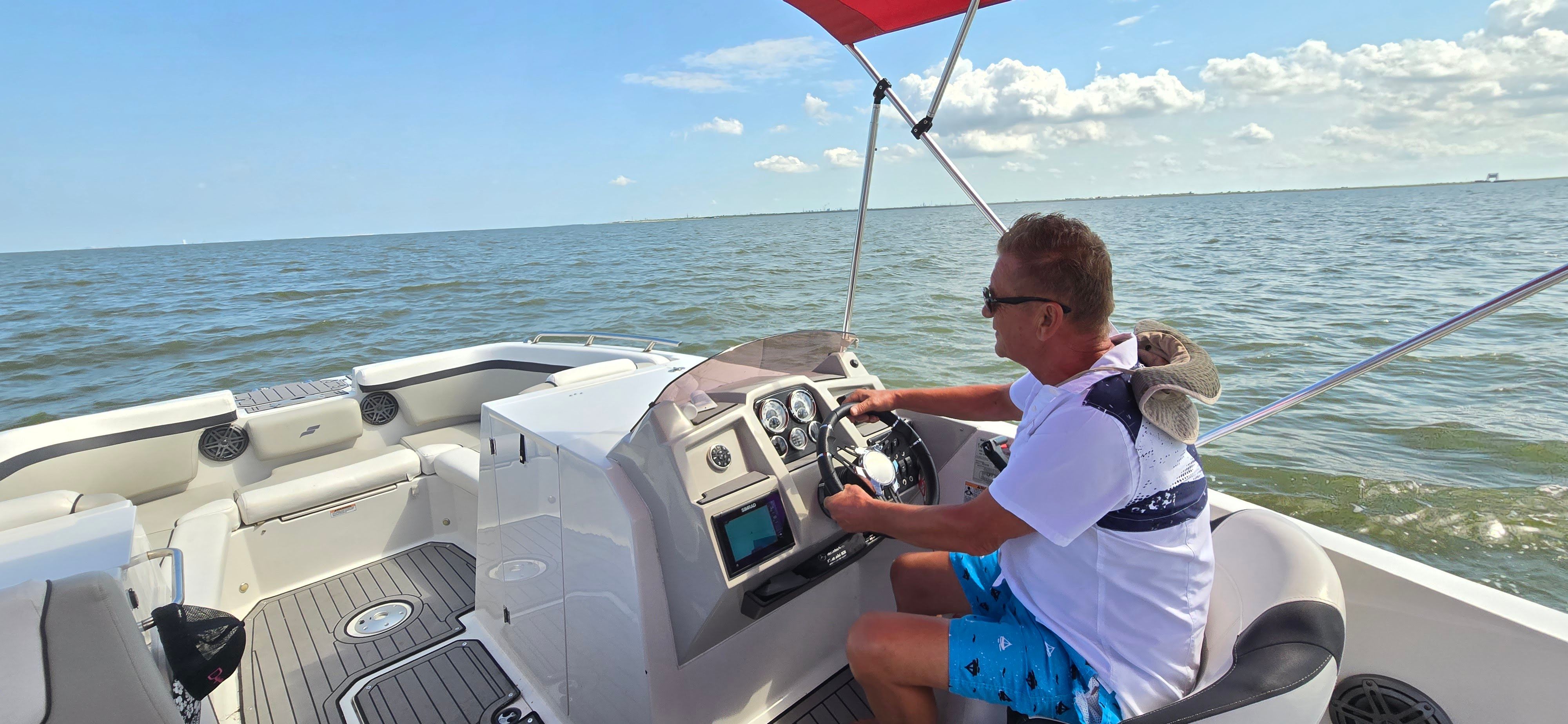 A man steers a Starcraft boat on calm water under a blue sky.