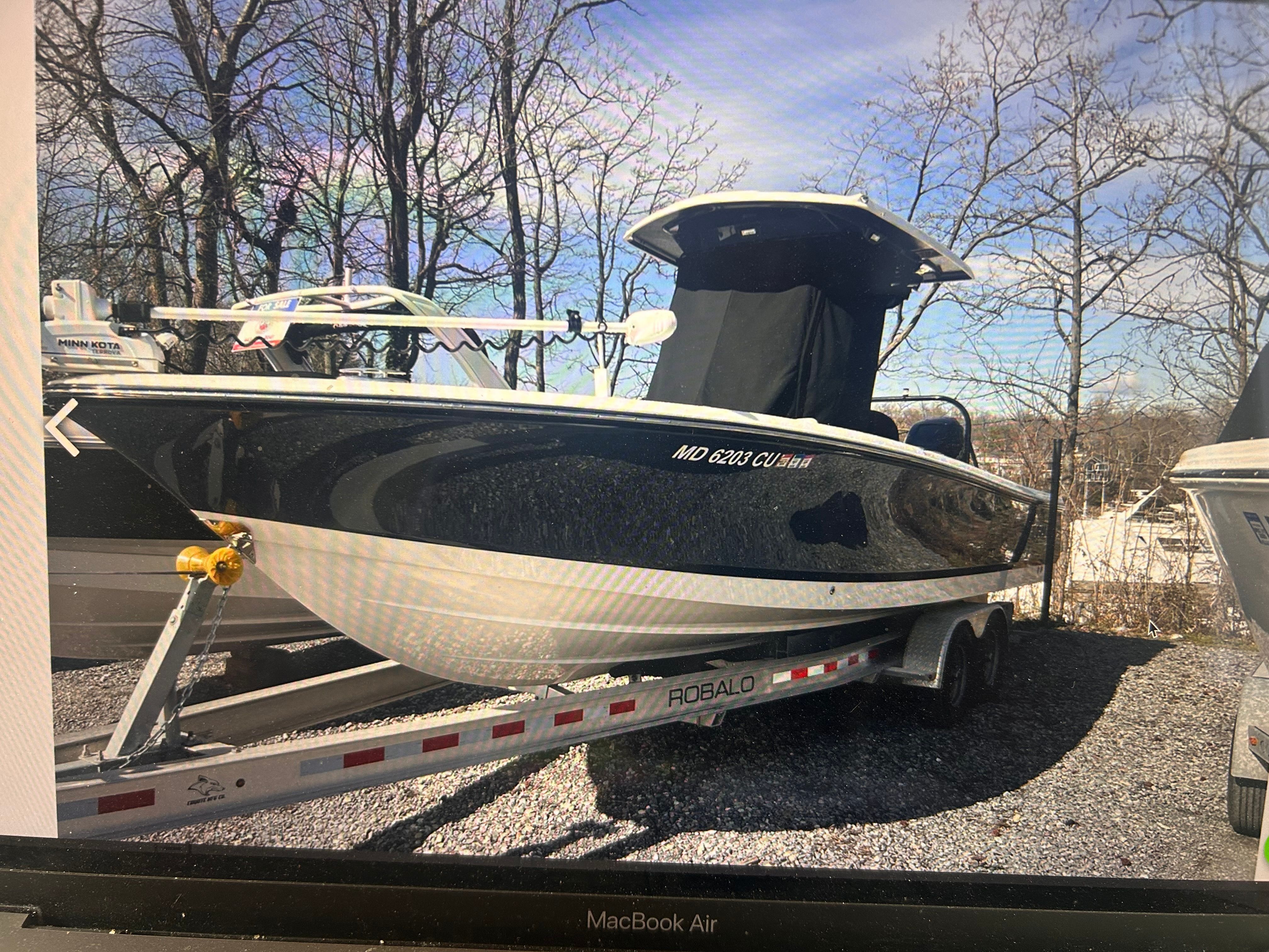 A 2023 Robalo 266 Cayman on a trailer, surrounded by trees.