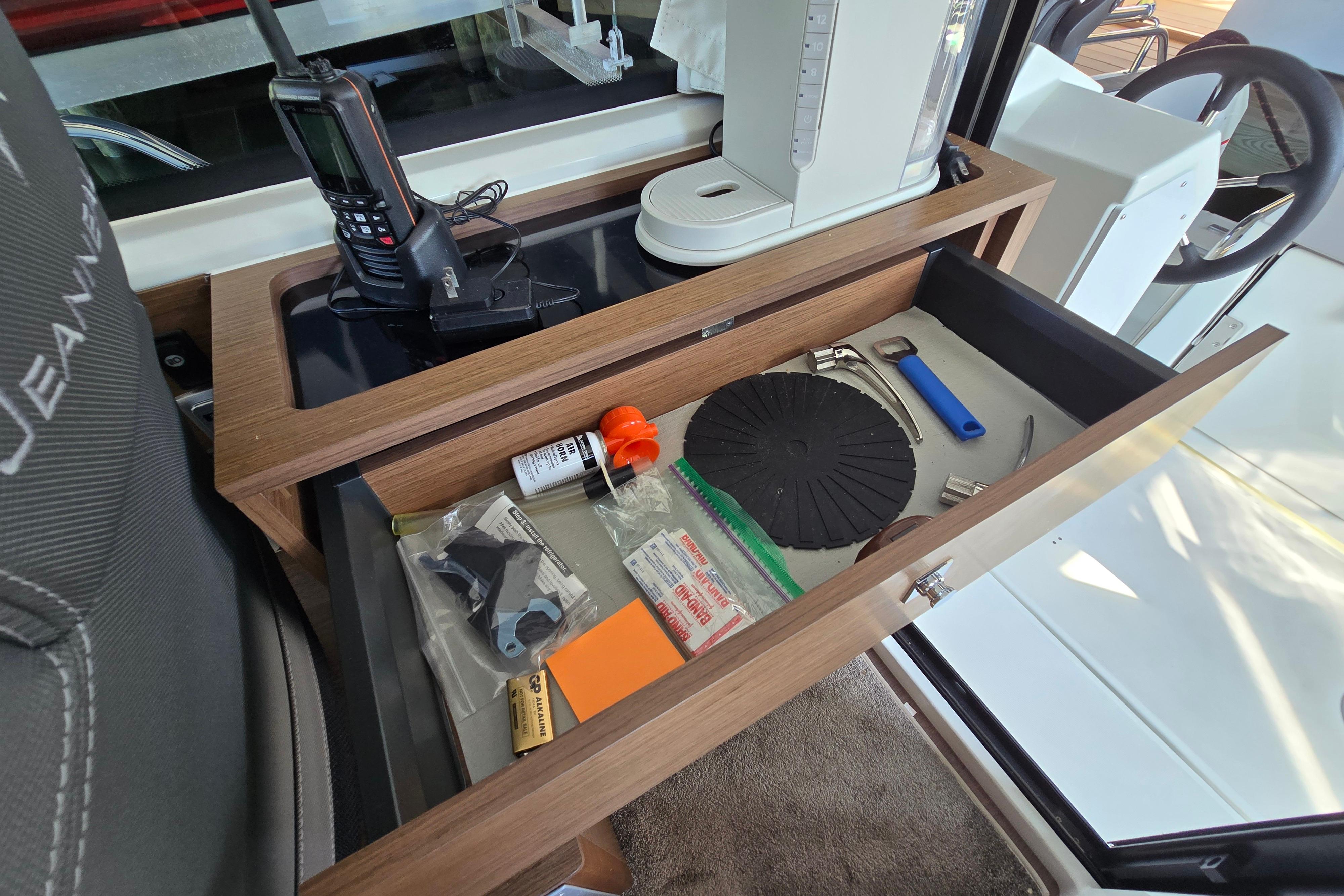 A drawer in a boat with tools and accessories, next to a radio.