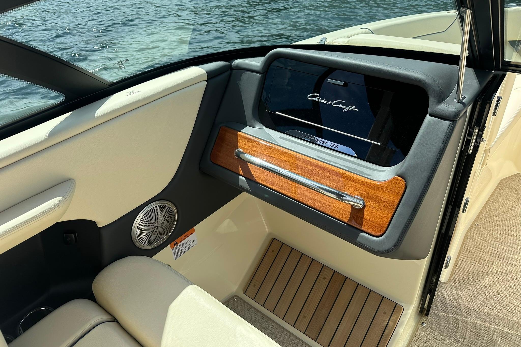 2026 Chris-Craft Sportster 25 interior with wood accents and speaker, near water.