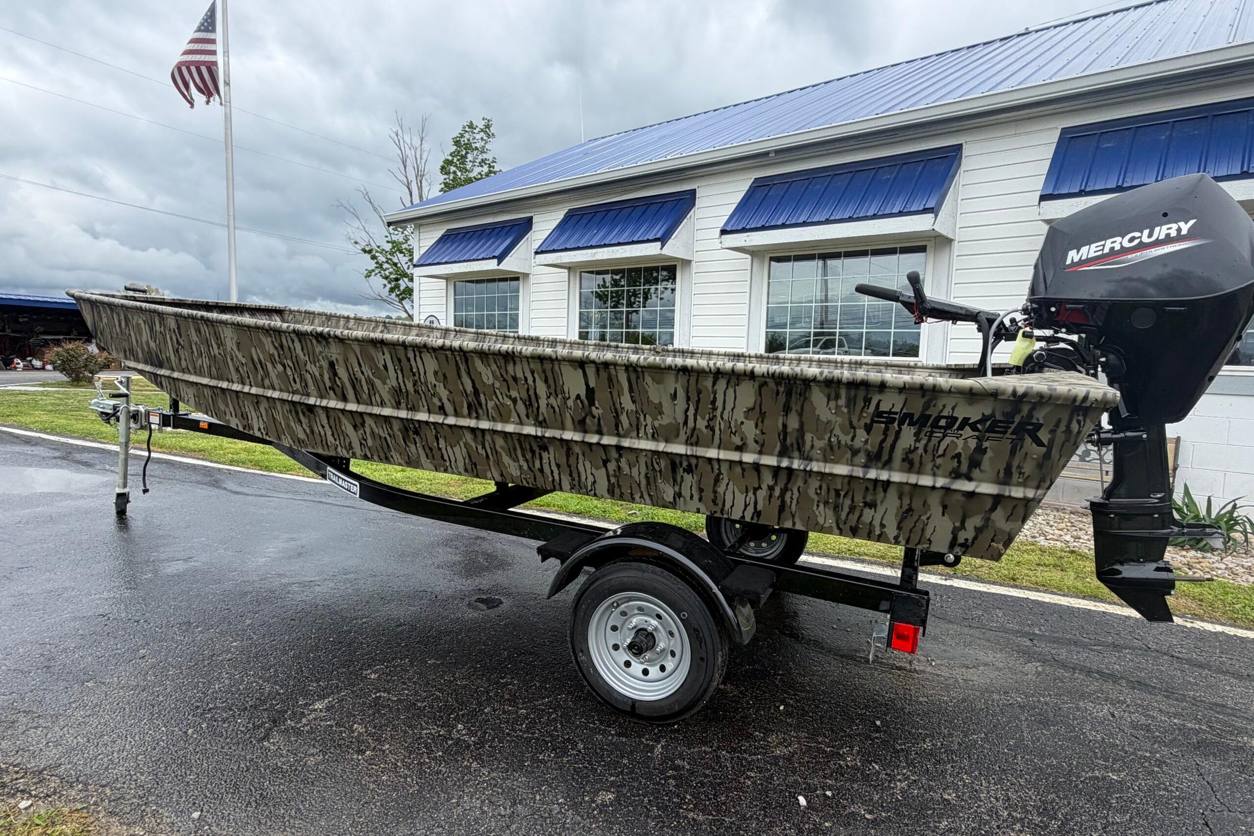 2026 Smoker Craft 1448 Jon boat with Mercury motor on trailer, parked outside a building.