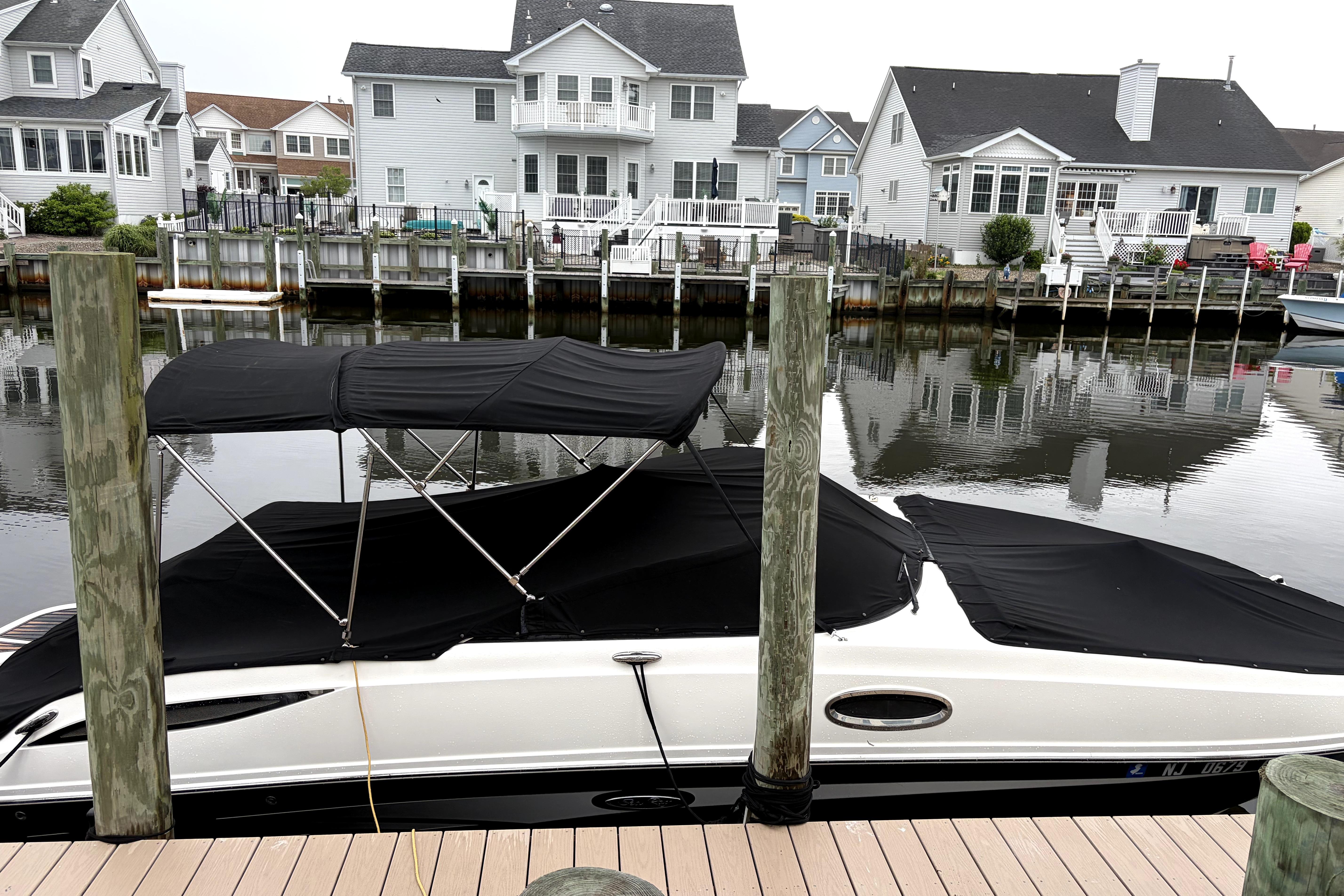 2014 Sea Ray 260 Sundeck docked by waterfront homes, covered with black canopy.