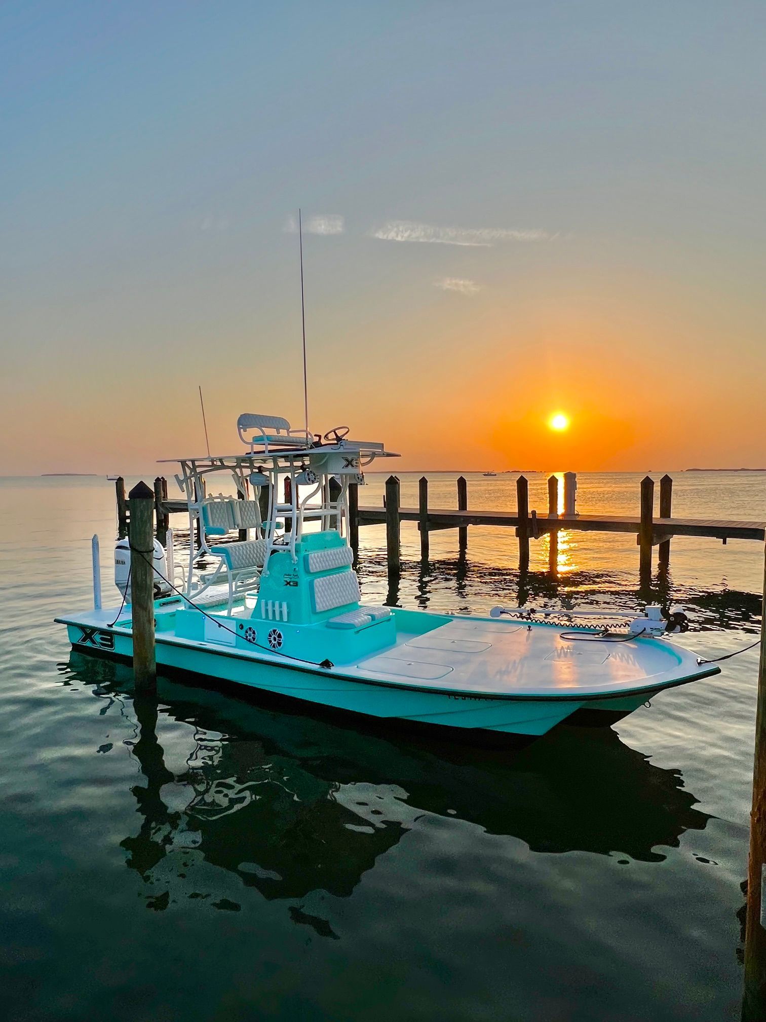 A turquoise boat docked at a pier during sunset.
