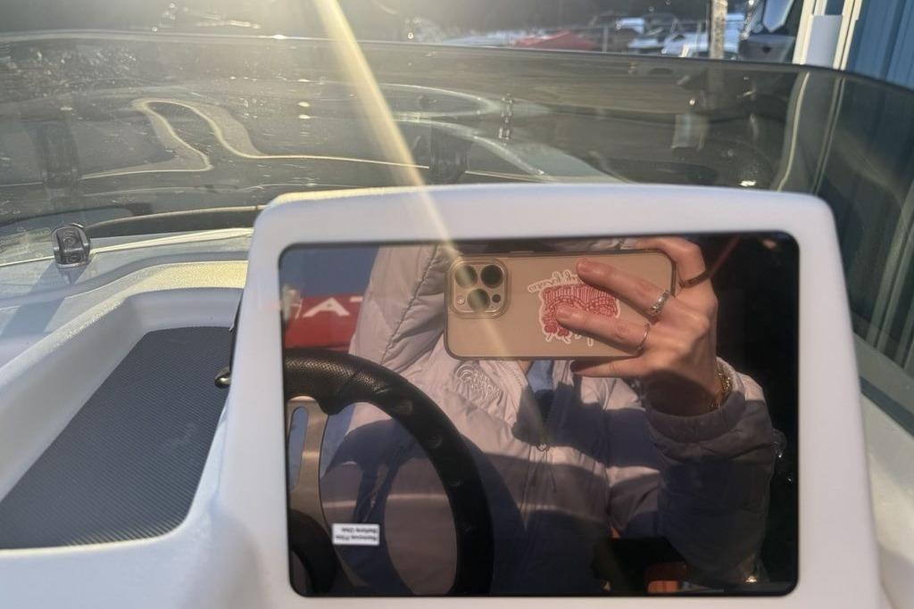 Reflection on Tahoe T16 boat dashboard, 2026 model, with smartphone in hand.