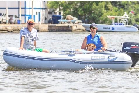 Two people and a dog on a 2024 Caribe c-10X inflatable boat on a sunny day.