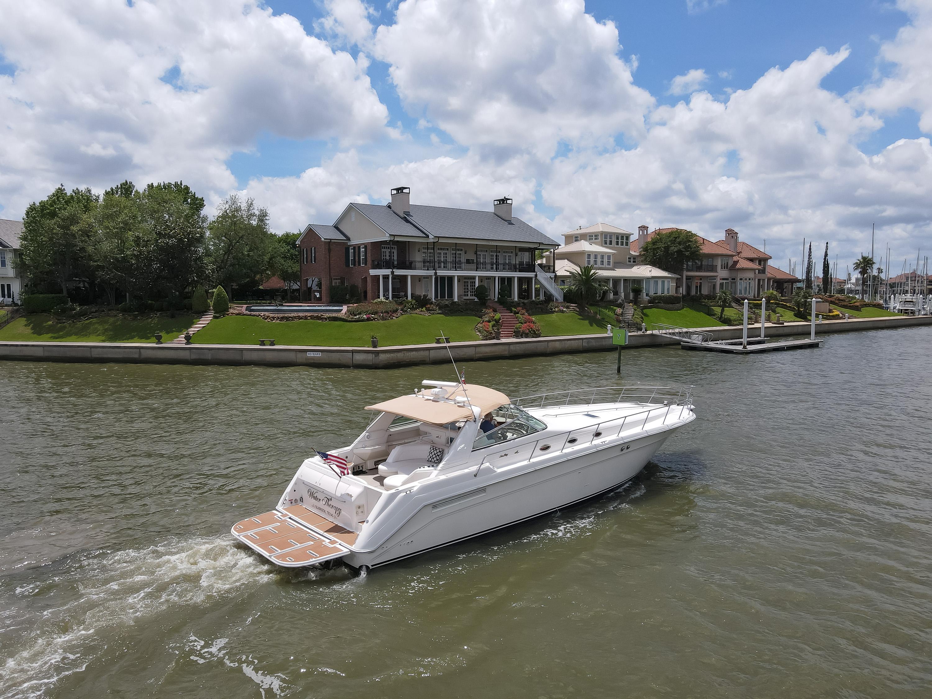 1996 Sea Ray 500 Sundancer cruising on a scenic river near luxury waterfront homes.