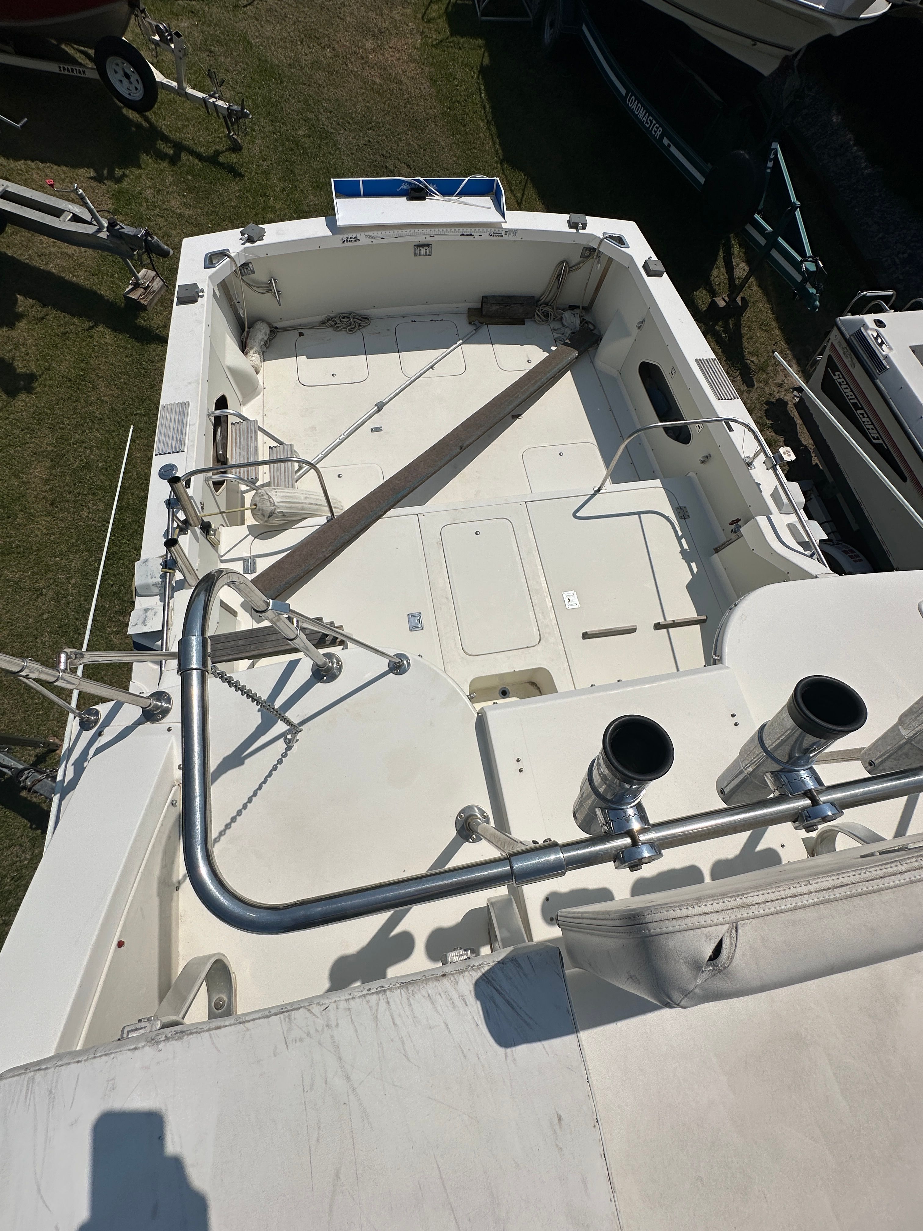 The image shows the spacious aft deck of a 1983 Bertram Flybridge Cruiser, featuring rod holders and storage.