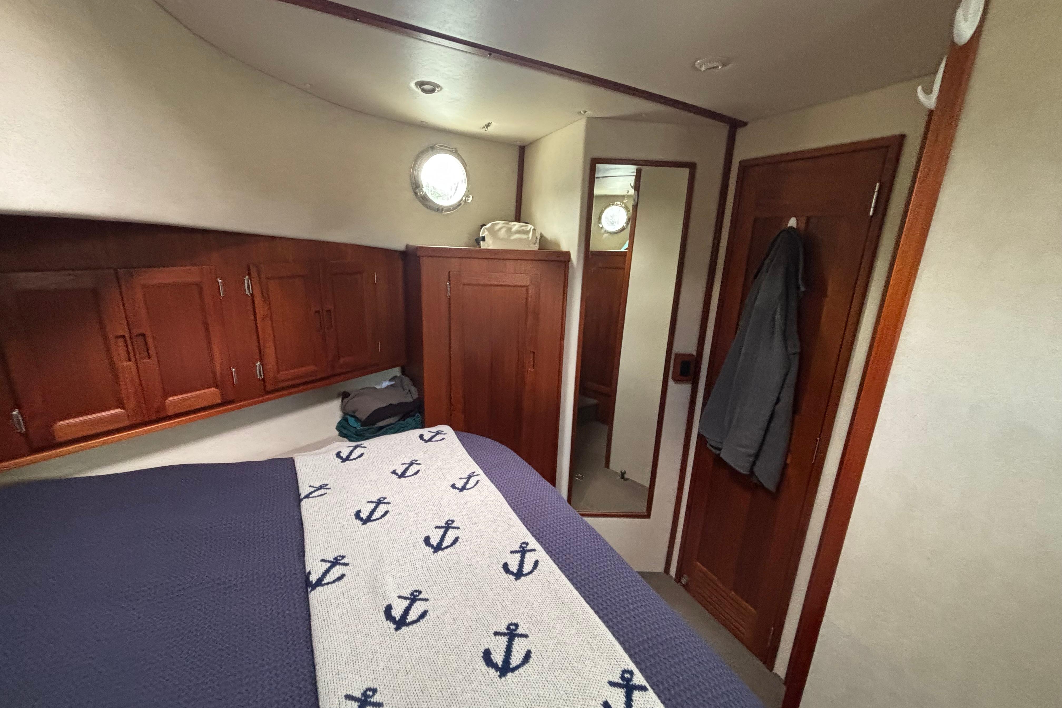 Cozy cabin interior of 2004 Nordic Tug 37 with nautical-themed bedding and wooden cabinetry.