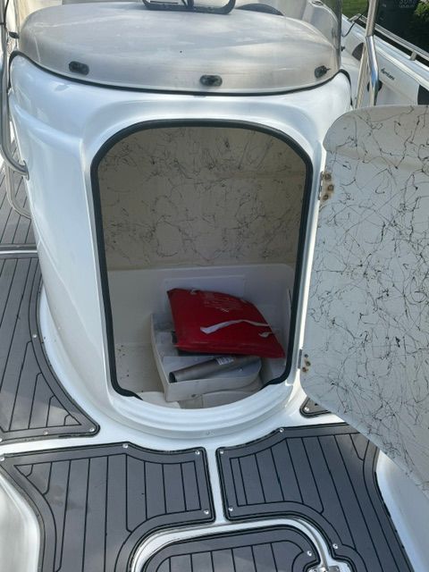 An open storage compartment on a boat with gray flooring and a red cushion inside.