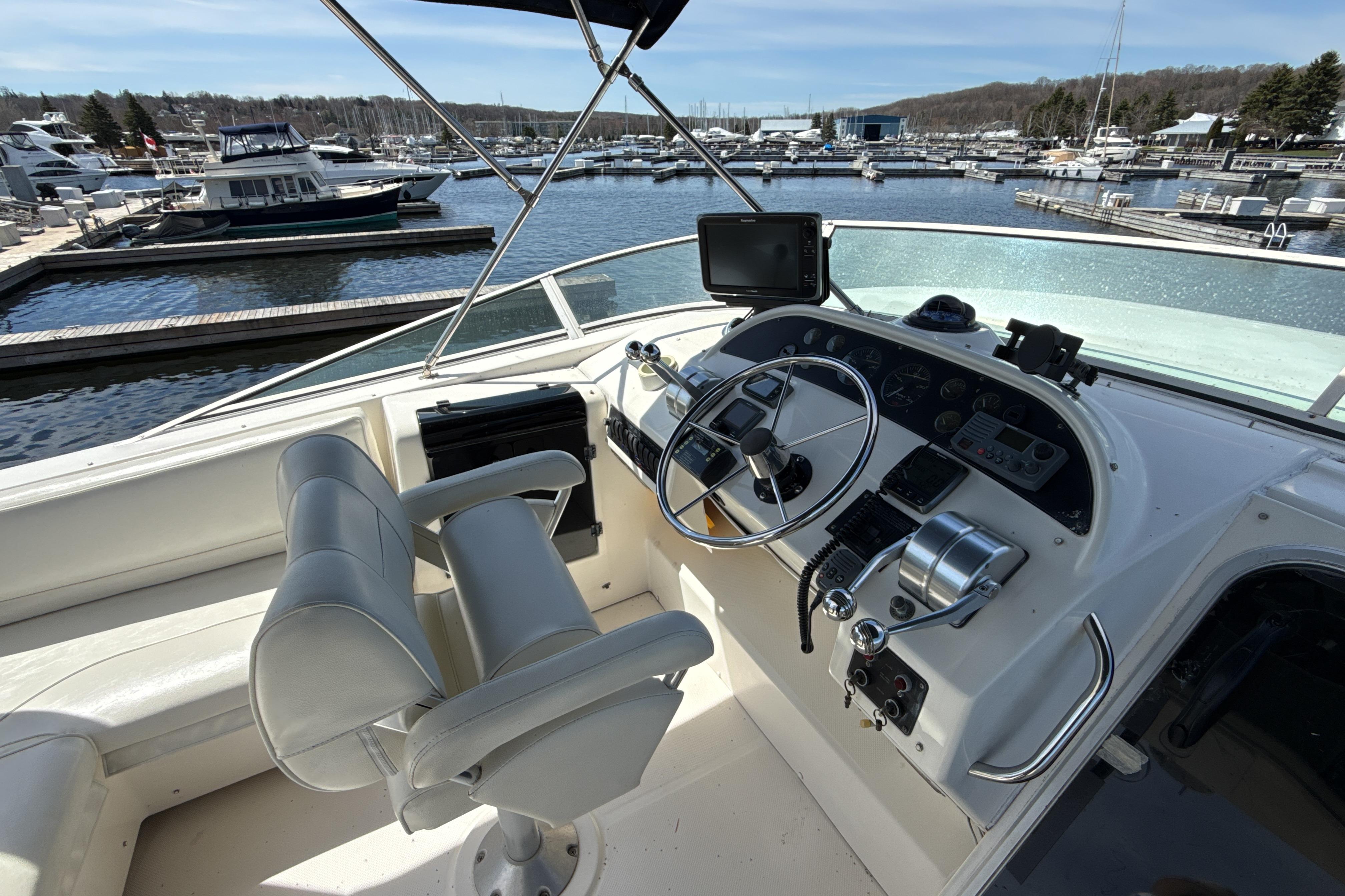 1997 Bayliner 4788 Pilot House Motoryacht helm with dual seats, steering wheel, and marina view.