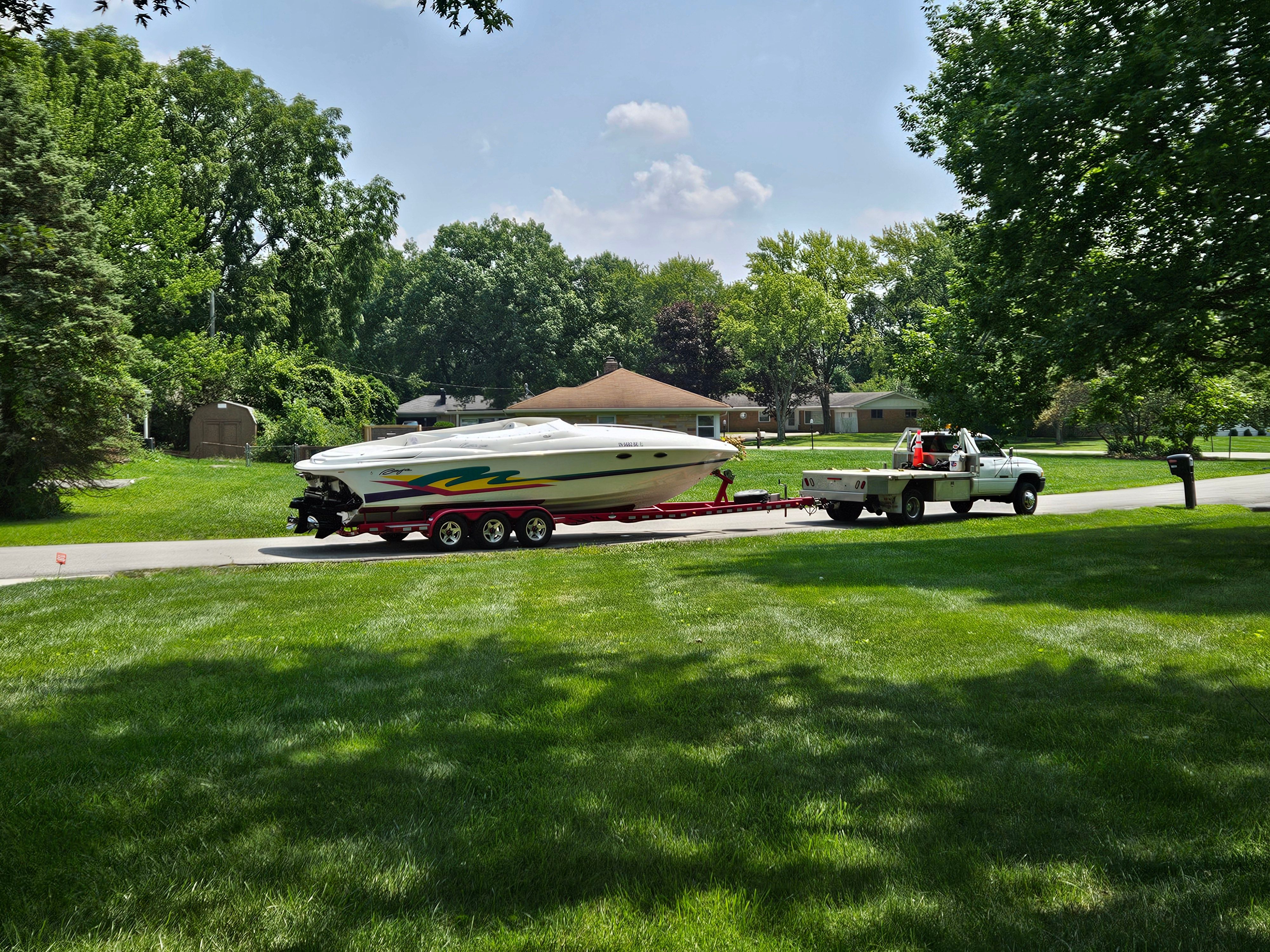 A 1996 Baja 302 Boss on a trailer, towed by a pickup truck in a green residential area.