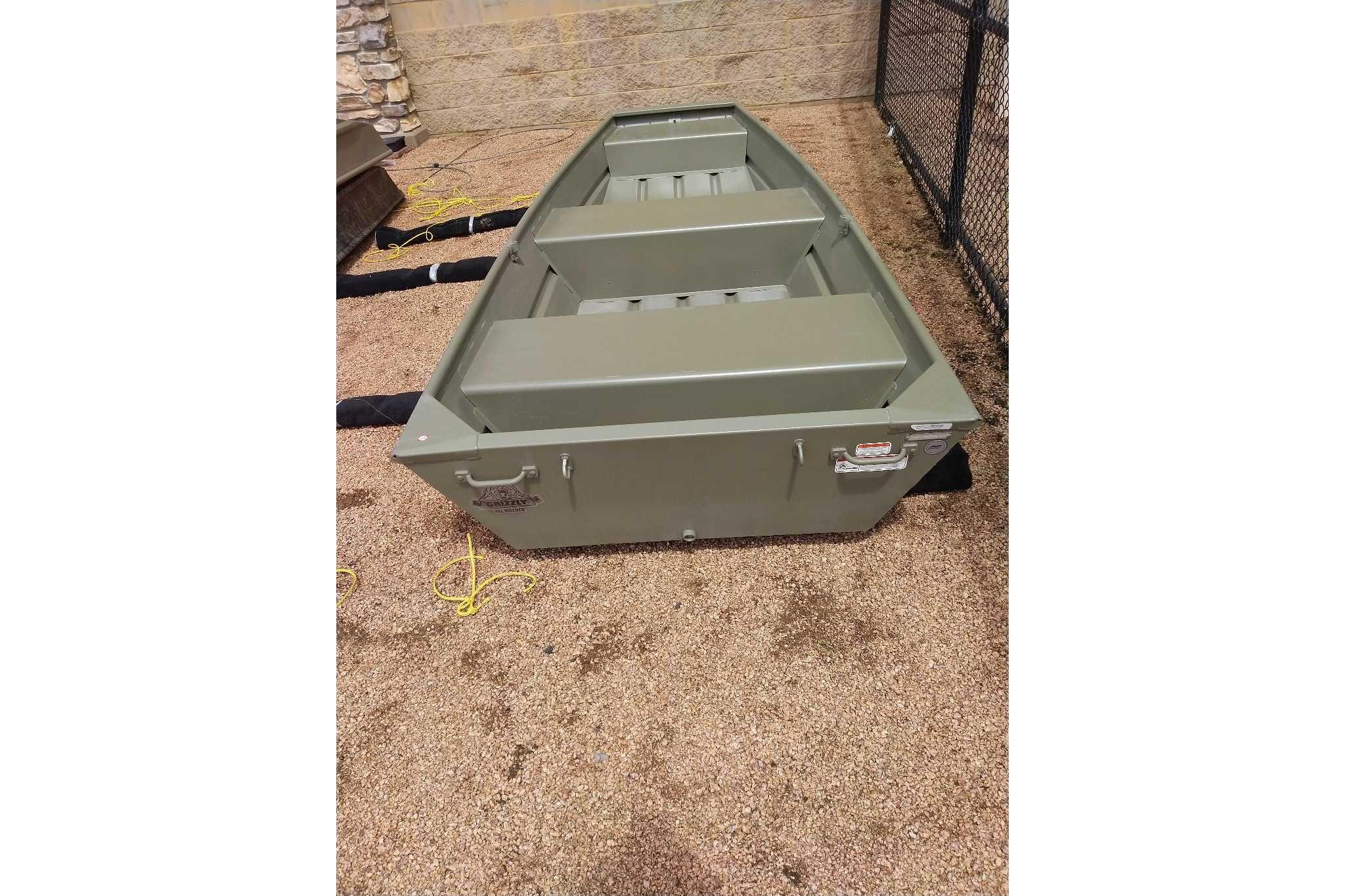 2026 Tracker Grizzly 12 Jon boat on gravel surface, featuring a sturdy, green aluminum design.