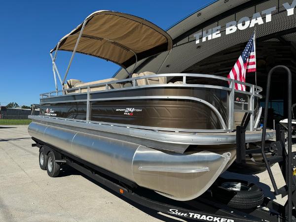 2025 Sun Tracker 24 Sportfish XP3 pontoon boat with canopy and American flag, parked on trailer.
