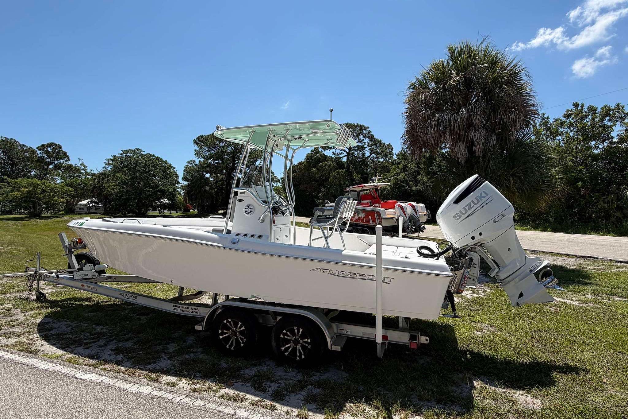 2022 Aquasport 230 Pro Bay boat on trailer with Suzuki outboard motor, parked outdoors.