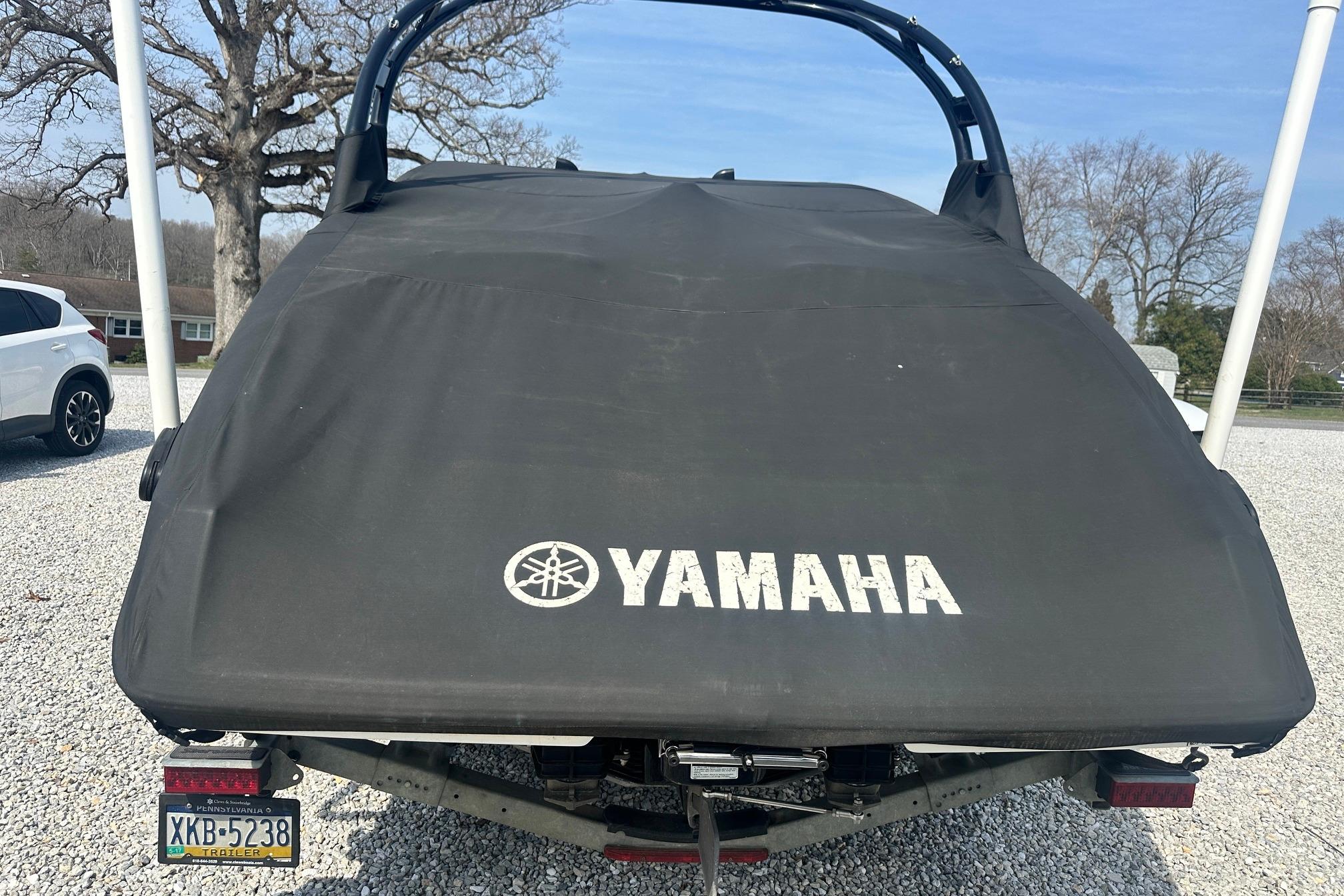 2016 Yamaha 242 Limited S boat covered, parked on gravel with trees in background.