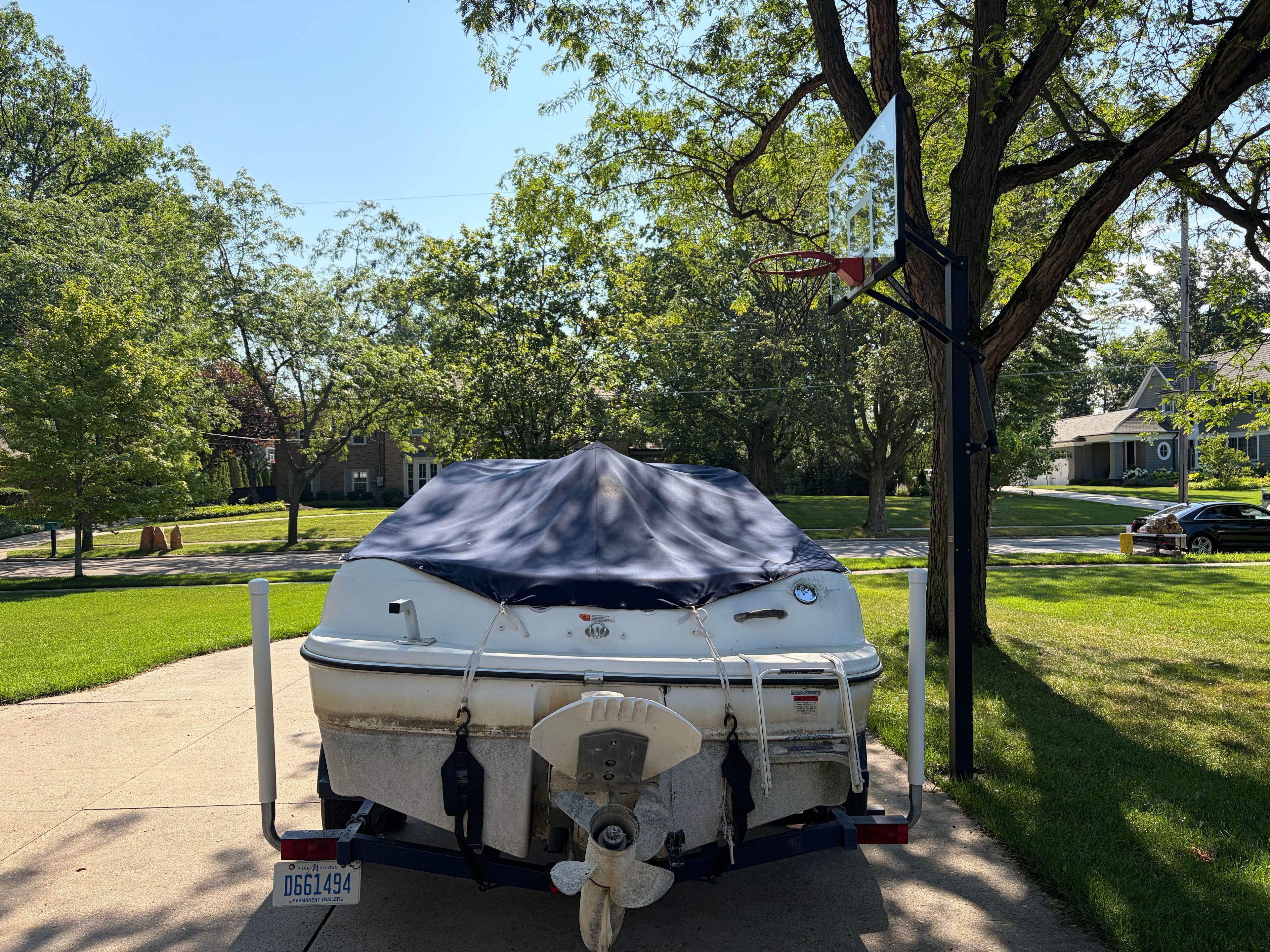 A 1999 Four Winns 170 Horizon boat on a trailer, covered, parked in a driveway.