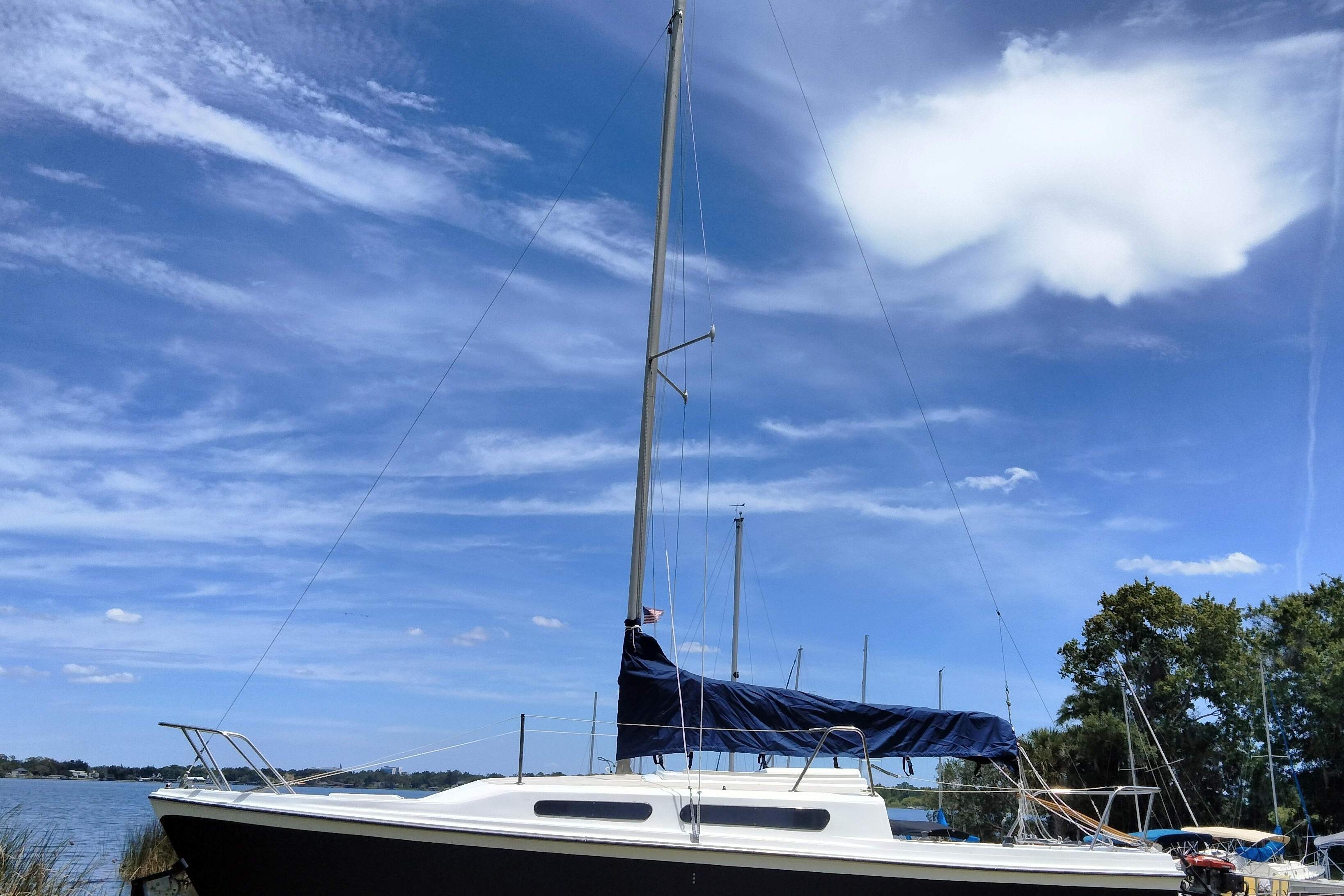 1980 MacGregor 25 sailboat docked under a clear blue sky with scattered clouds.