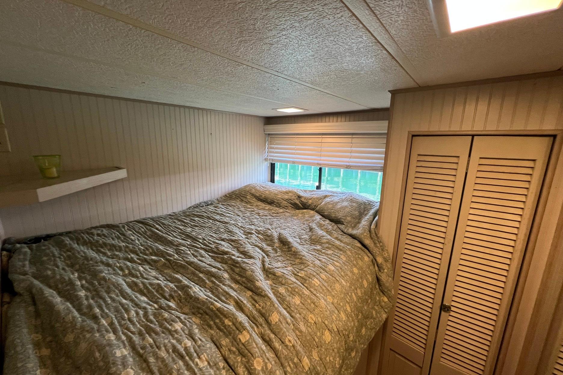Cozy bedroom interior of a 1993 Sumerset houseboat with a bed and wooden closet.