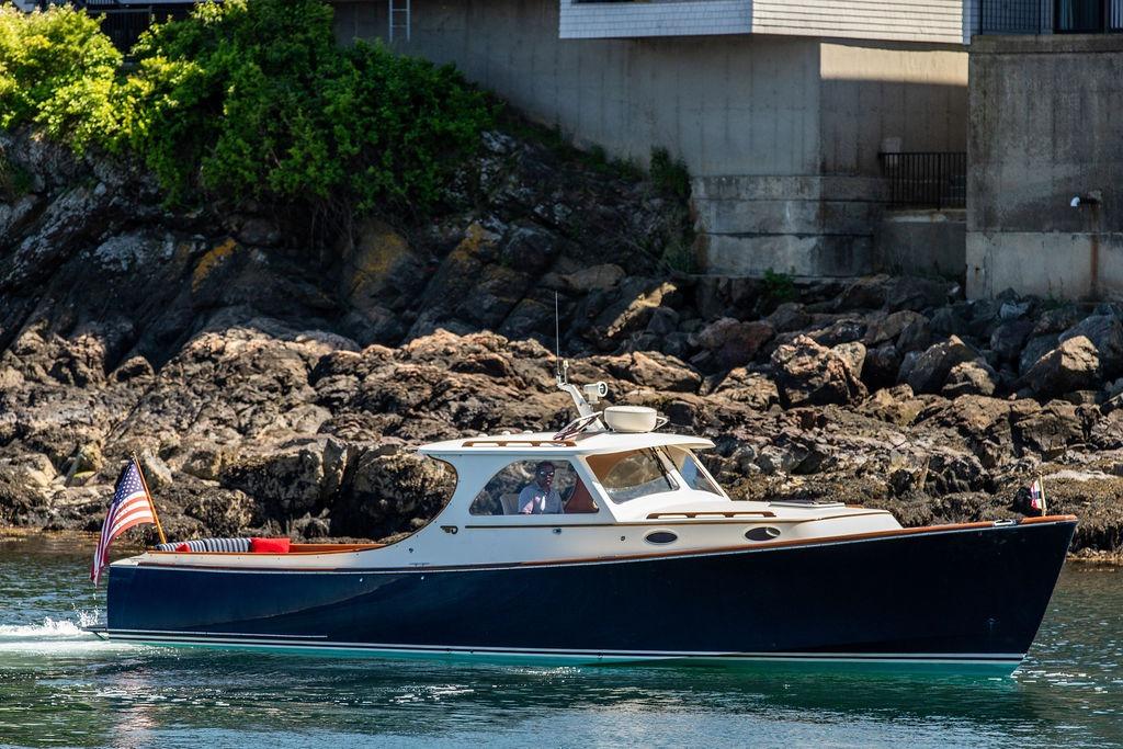 Hinckley Picnic Boat 36 Classic 2000 cruising near rocky shoreline with American flag.
