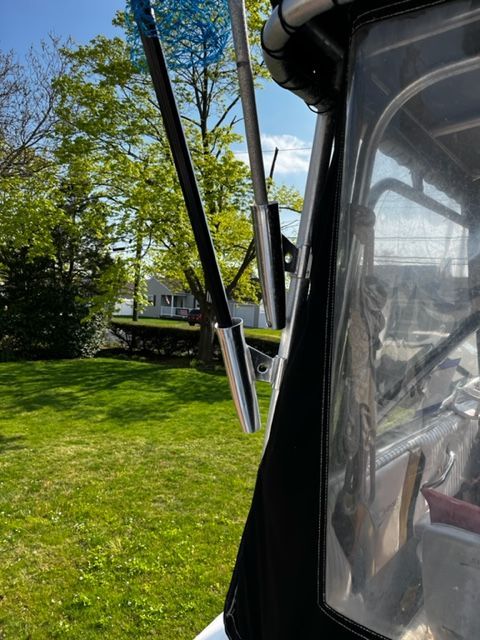 Part of a boat with fishing rod holders and a clear sky in the background.