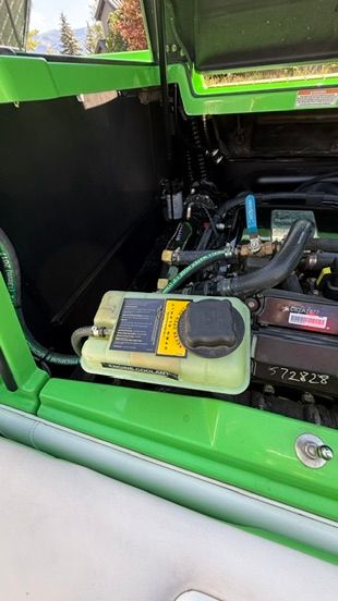 The engine compartment of a green boat shows hoses and a fluid reservoir.