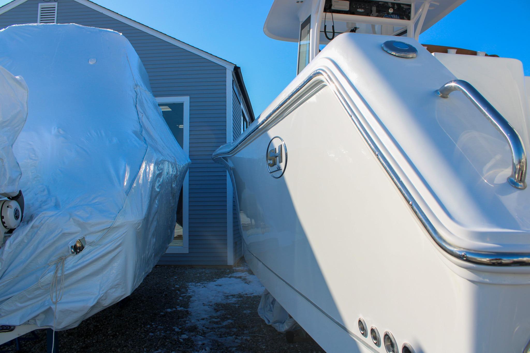 2026 Sea Hunt Gamefish 25 boat beside a covered vessel, near a building.