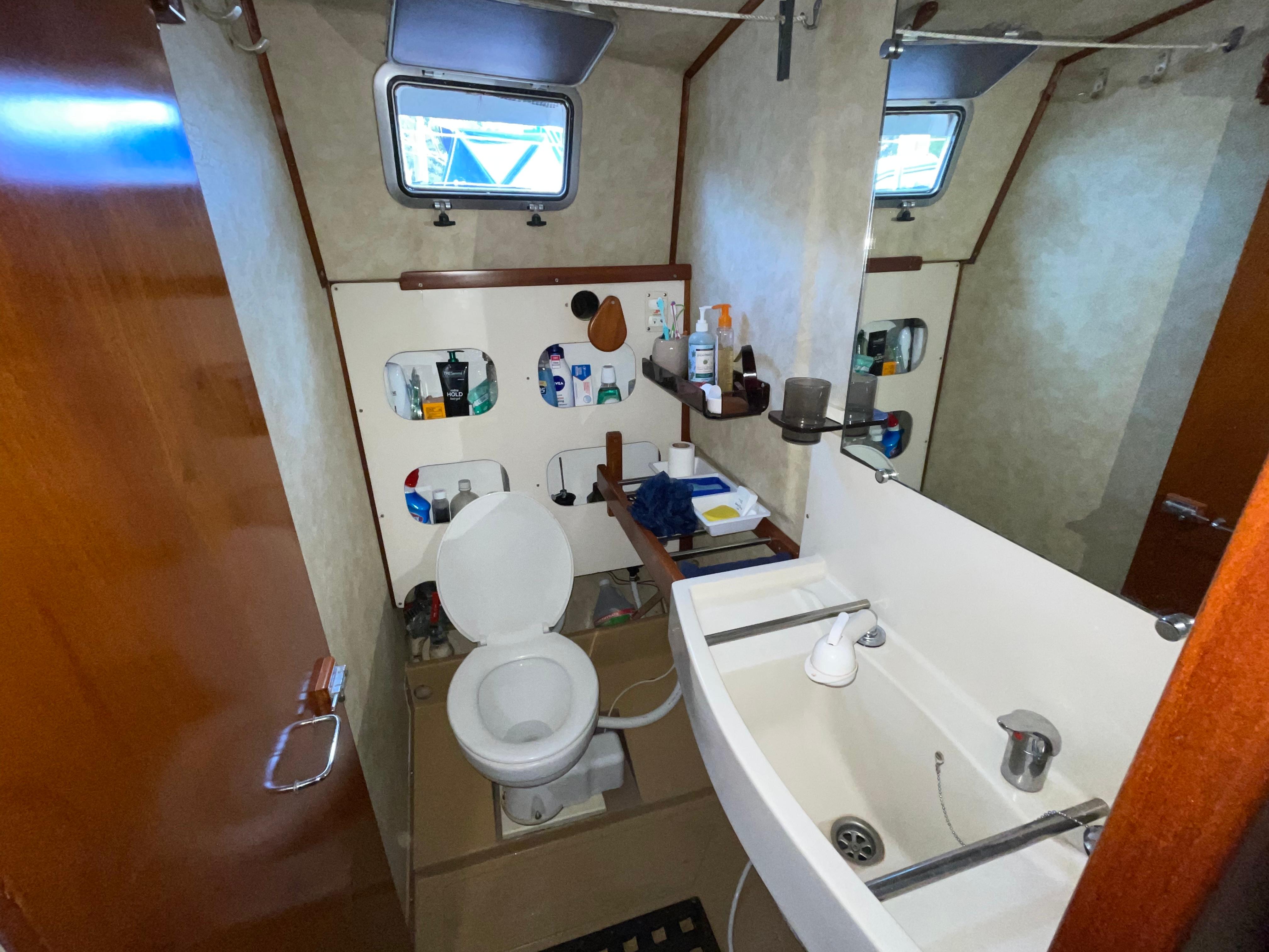Bathroom interior of 1985 Amel Maramu yacht with sink, toilet, and storage shelves.