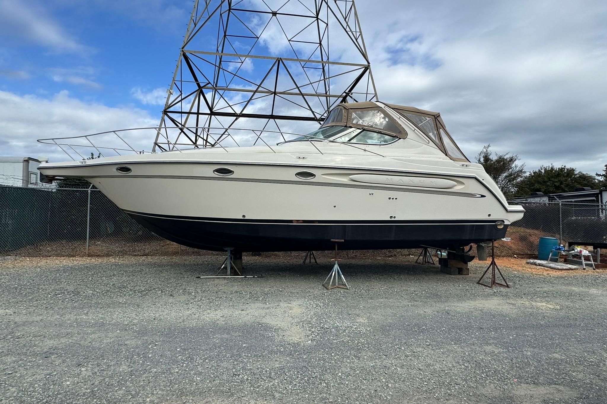 1998 Maxum 3700 SCR boat on stands, outdoor storage, overcast sky.