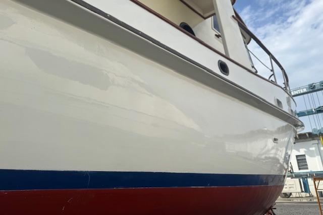 1986 Krogen 42 Classic boat with white hull and blue-red stripe, docked under a cloudy sky.