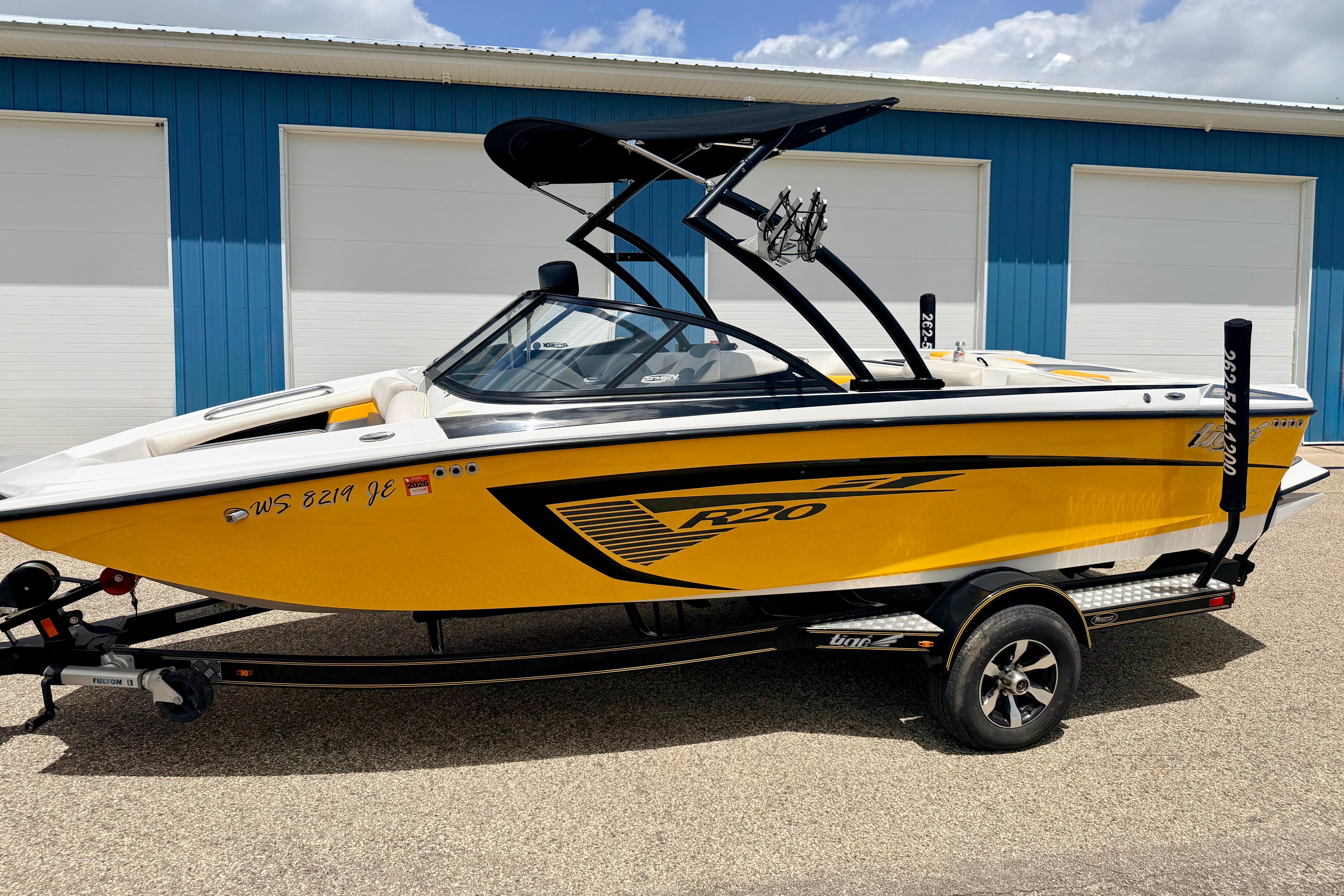 2014 Tigé R20 yellow boat on trailer, parked outside blue building.