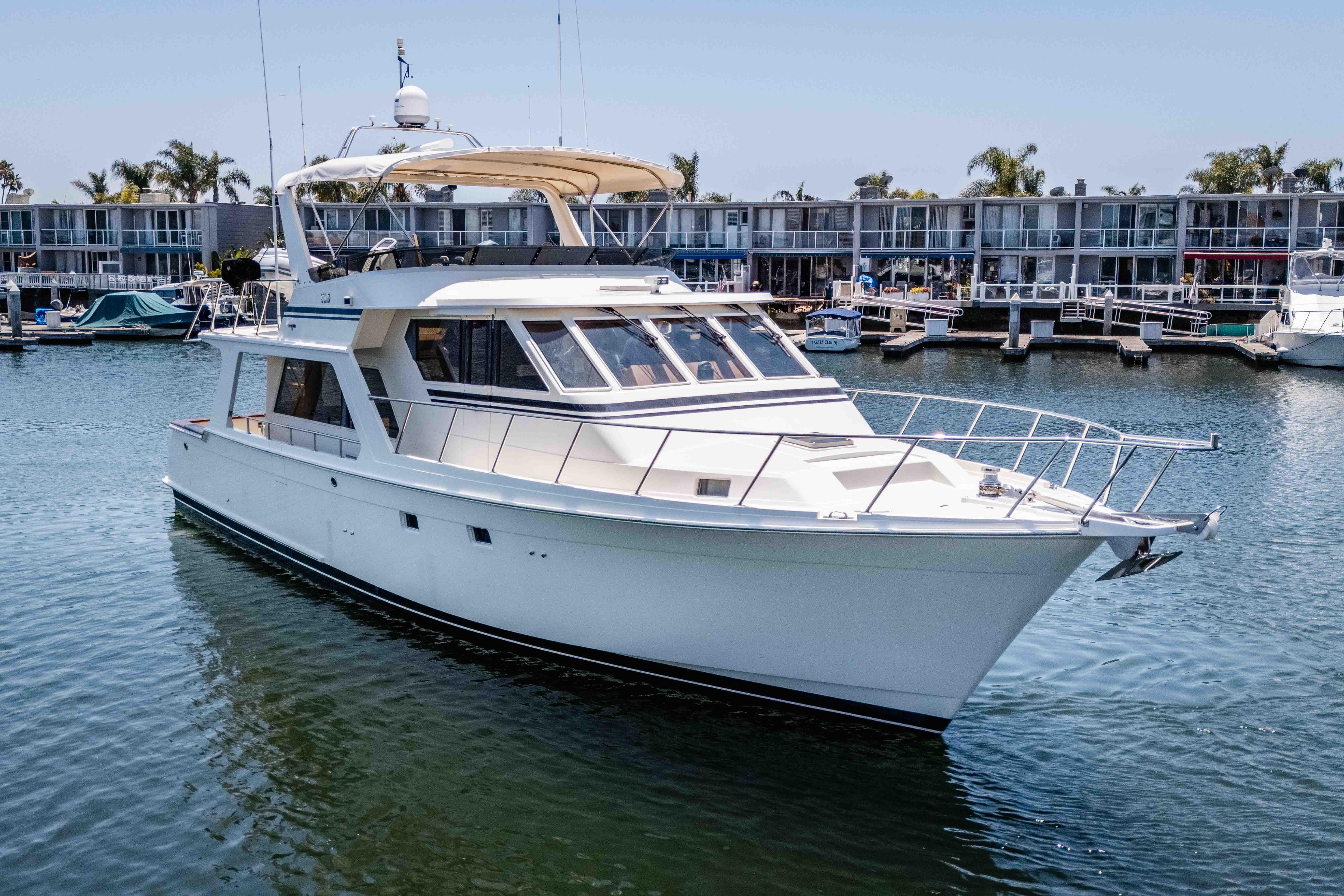 2005 Offshore Yachts 54 Pilothouse cruising in a marina, surrounded by modern waterfront buildings.