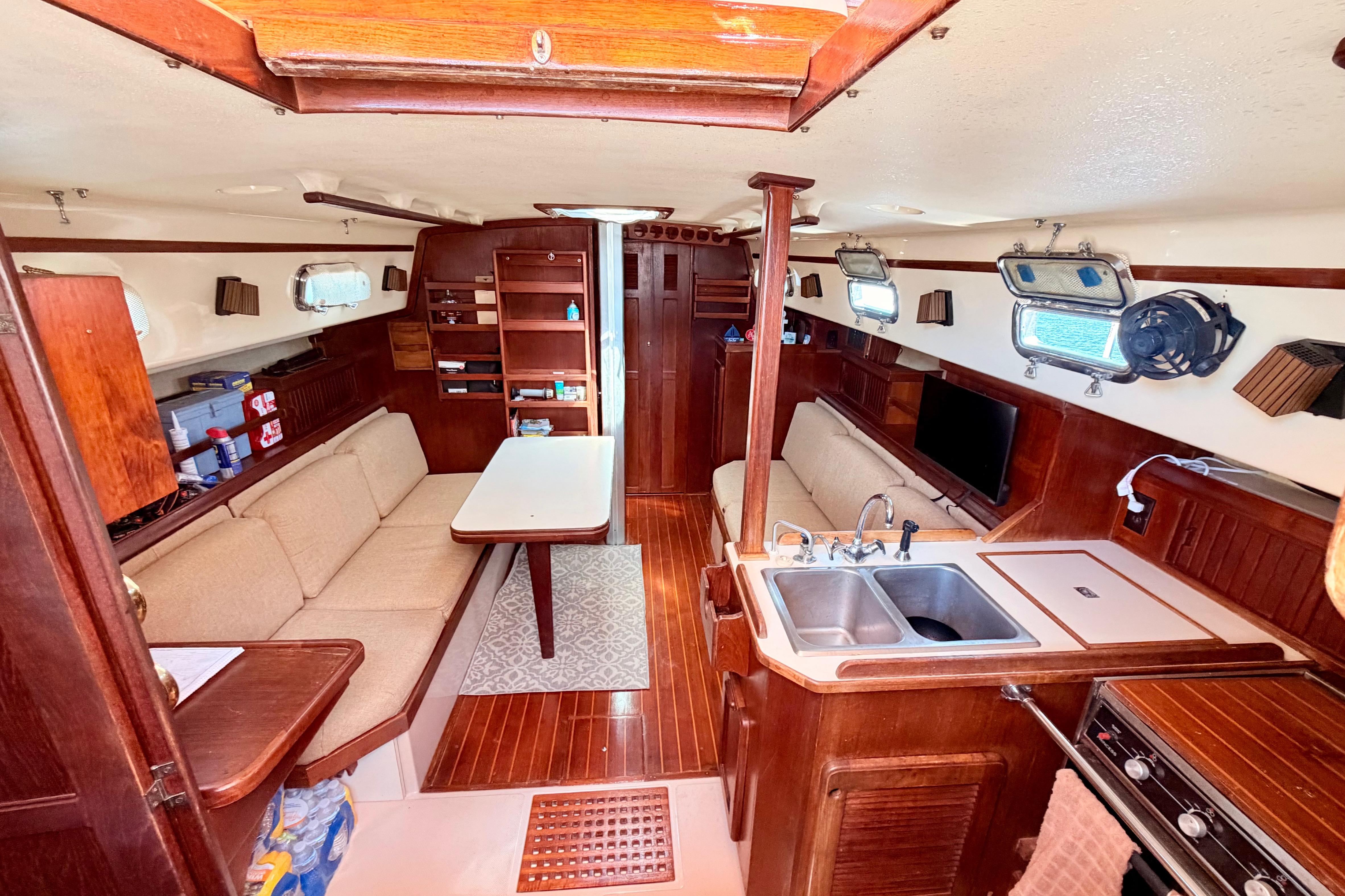1989 Island Packet Cutter interior with wood finish, cozy seating, and compact kitchen area.