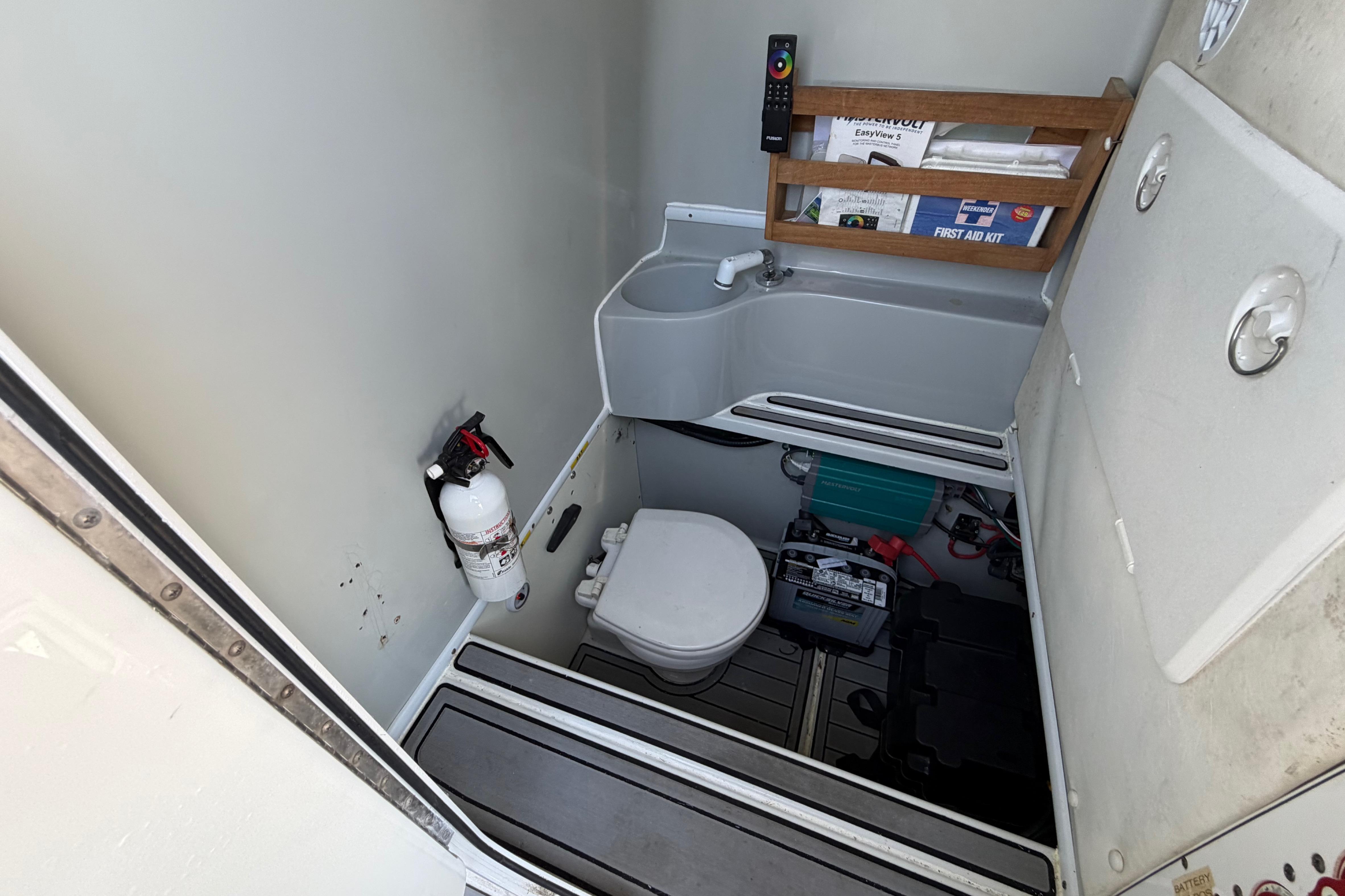 2015 Contender 32 ST boat bathroom with toilet, sink, fire extinguisher, and first aid kit.
