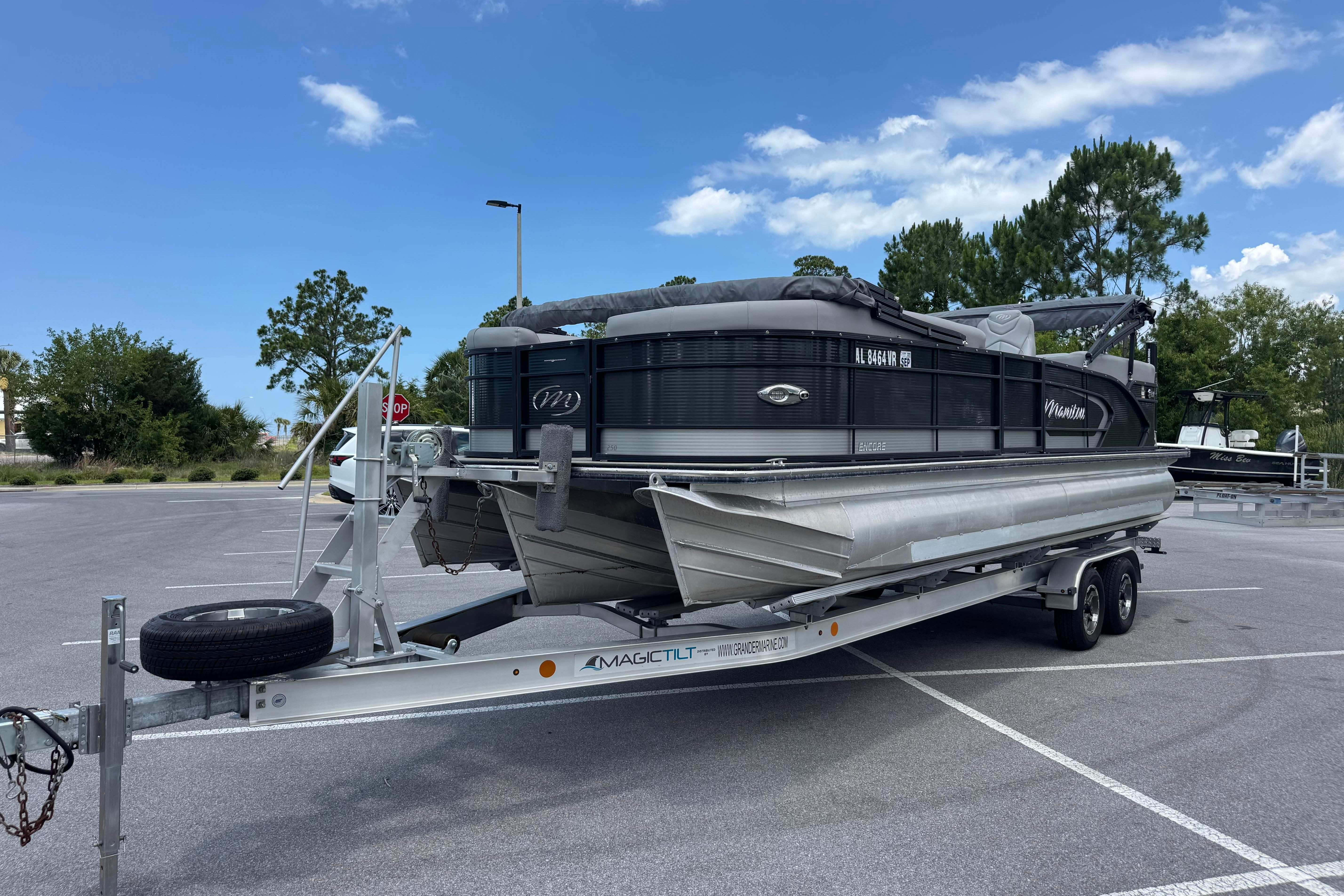 2022 Manitou 25 Encore pontoon boat on trailer in parking lot under blue sky.
