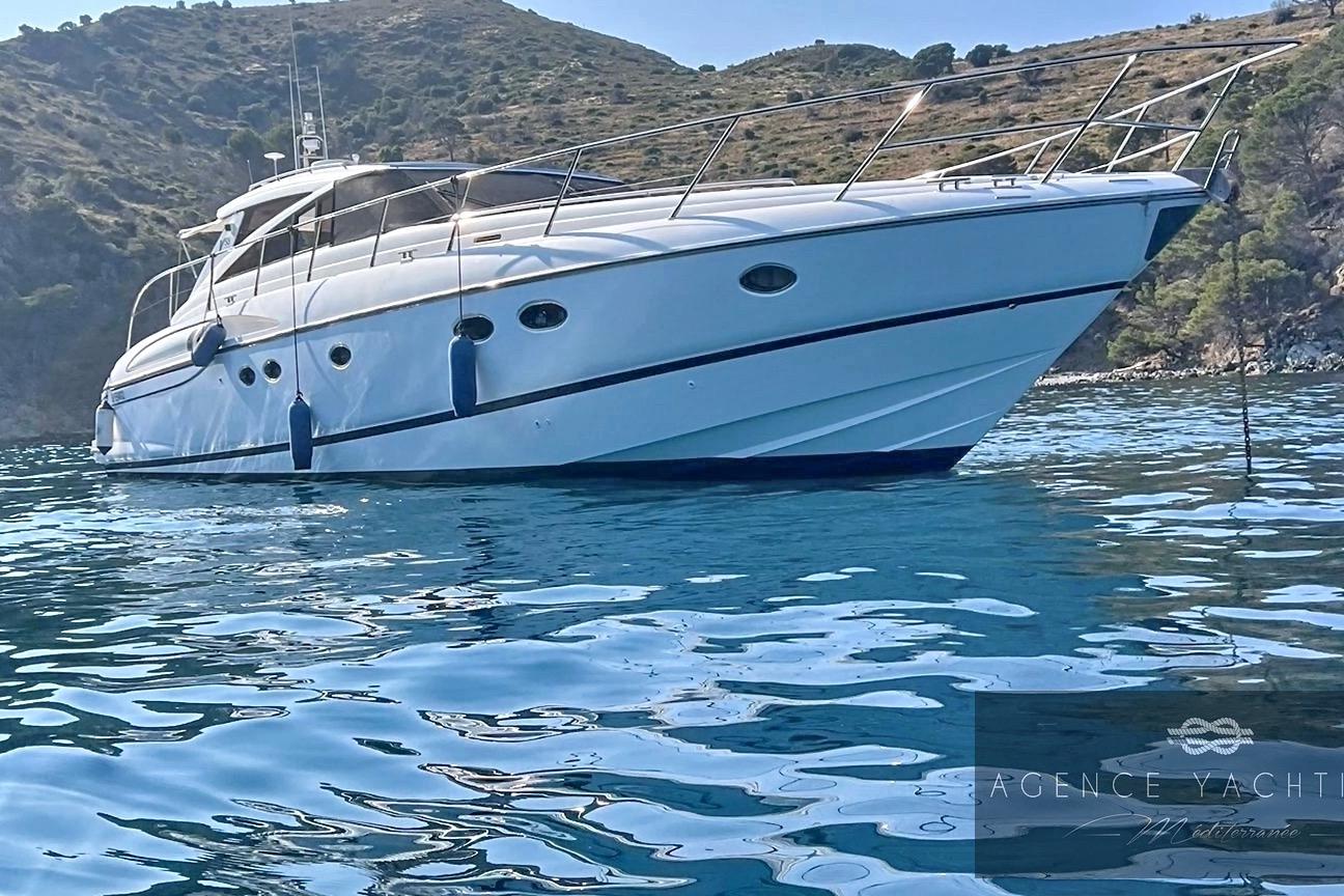 2004 Princess V58 yacht anchored in clear blue water near rocky coastline.