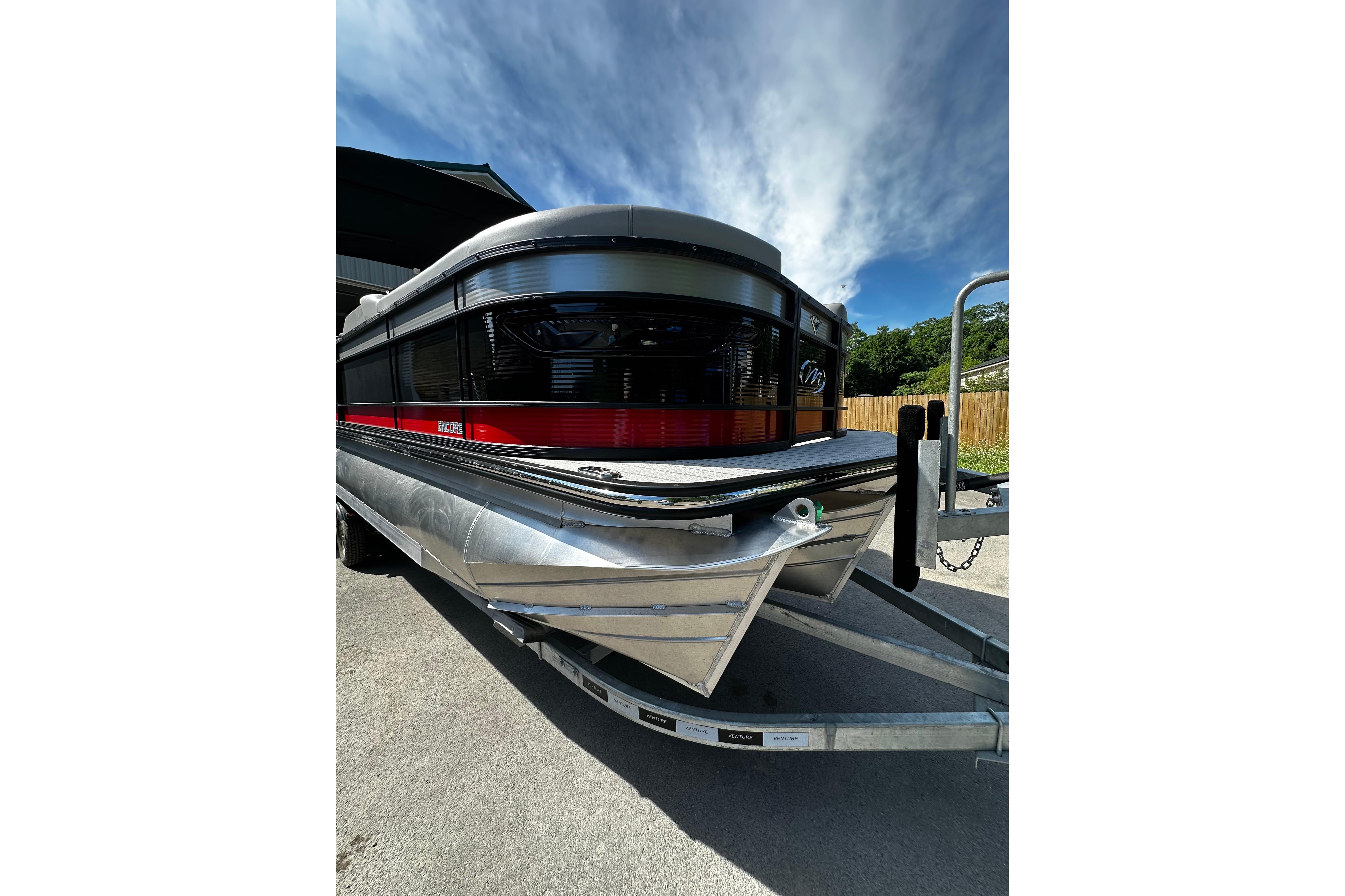 2027 Manitou 25 Encore RF pontoon boat on trailer under a clear blue sky.