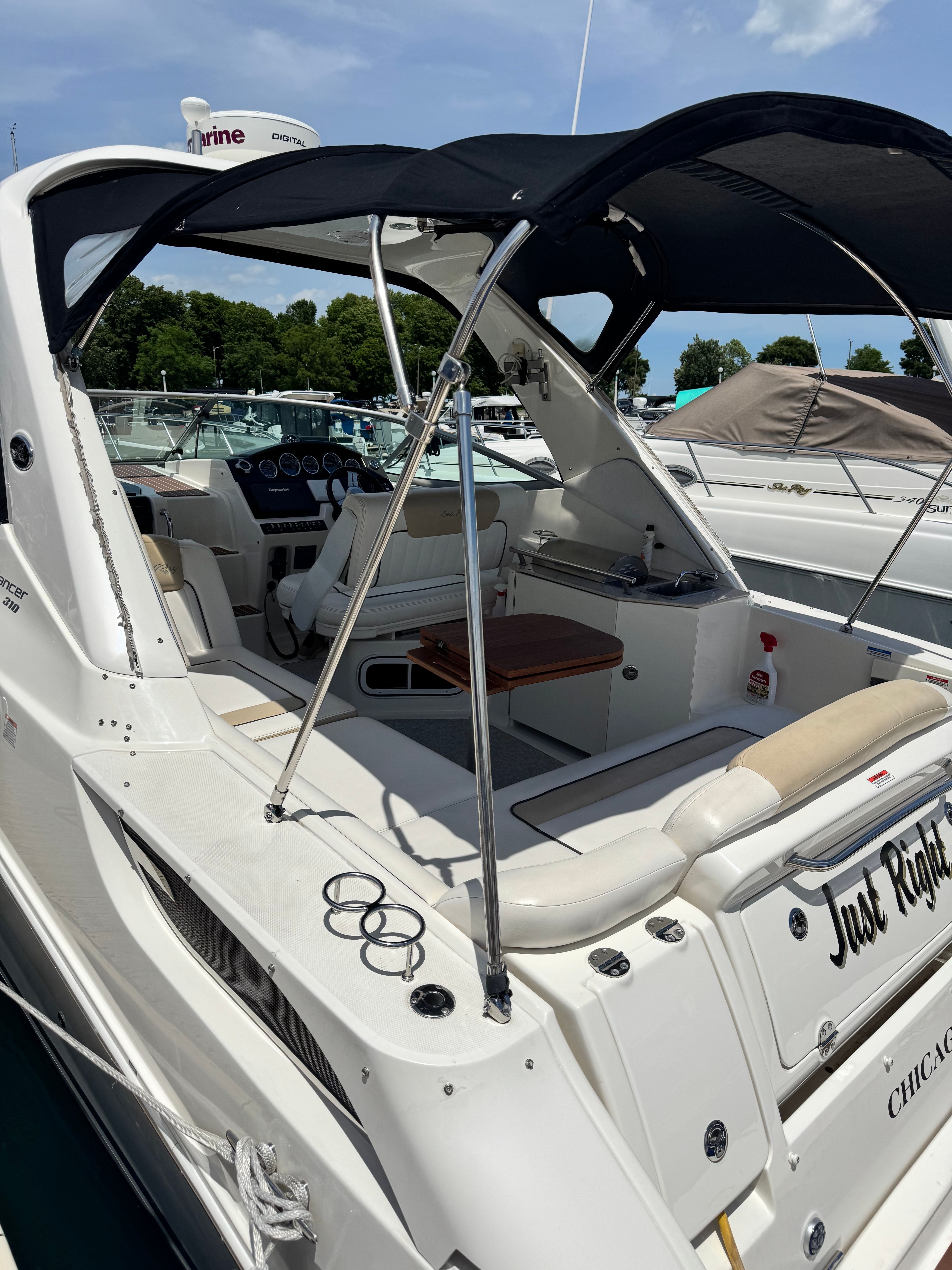 A 2010 Sea Ray Sundancer 310 with an open cockpit and black sunshade, docked in a marina.