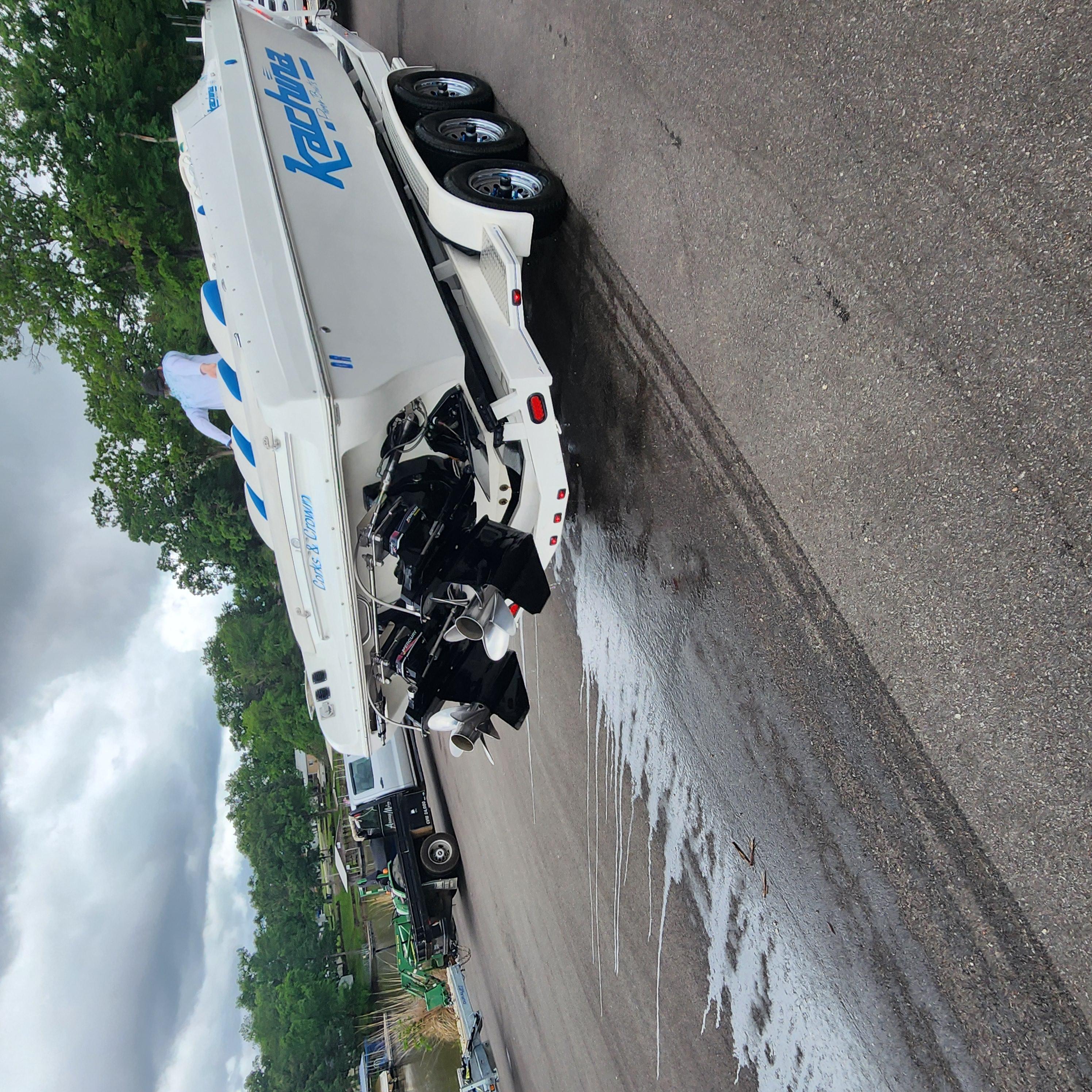 2005 Kachina Bolero boat on trailer, parked on wet pavement, surrounded by trees.