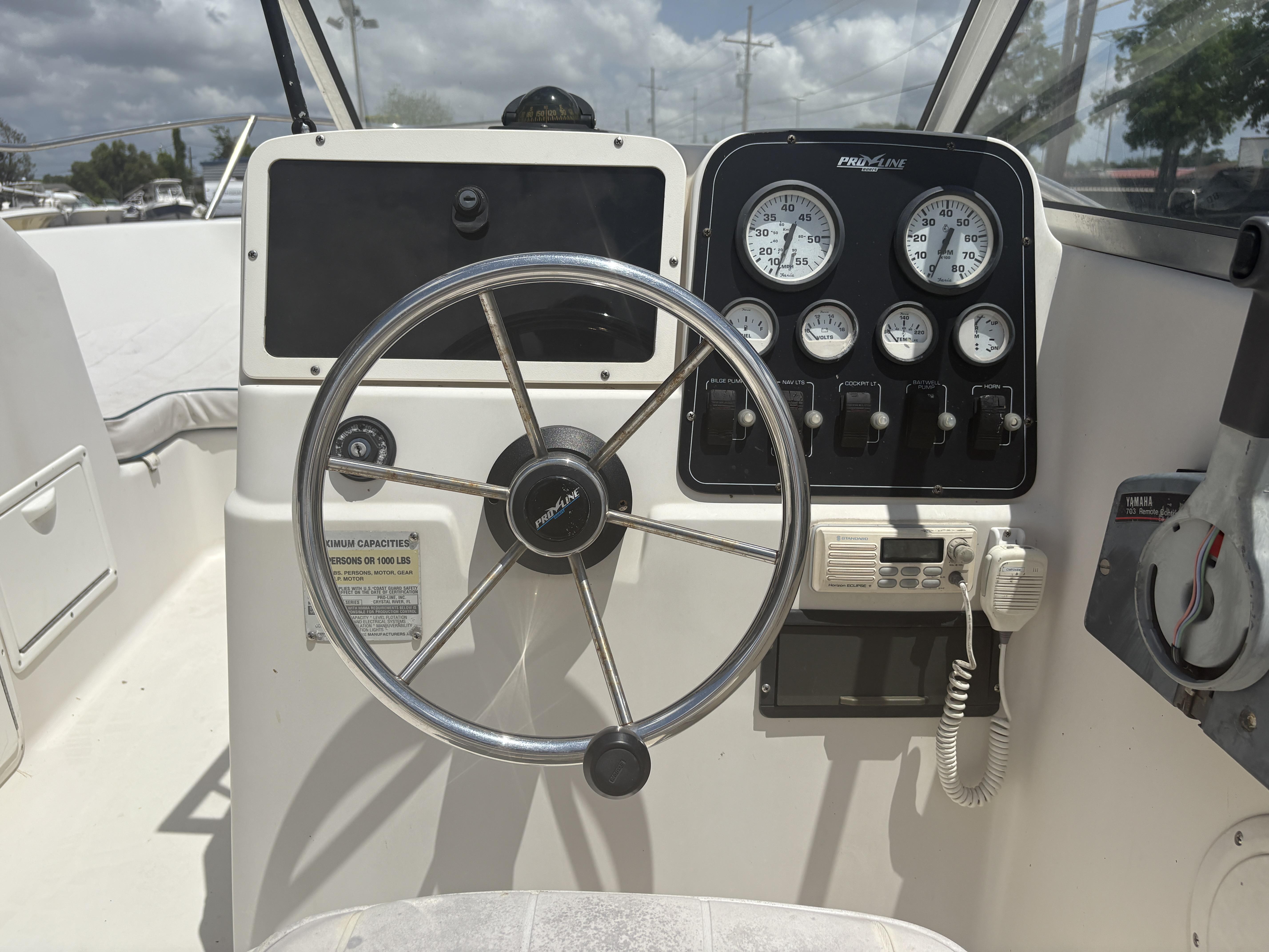 1996 Pro-Line 202 boat dashboard with steering wheel and gauges under a cloudy sky.