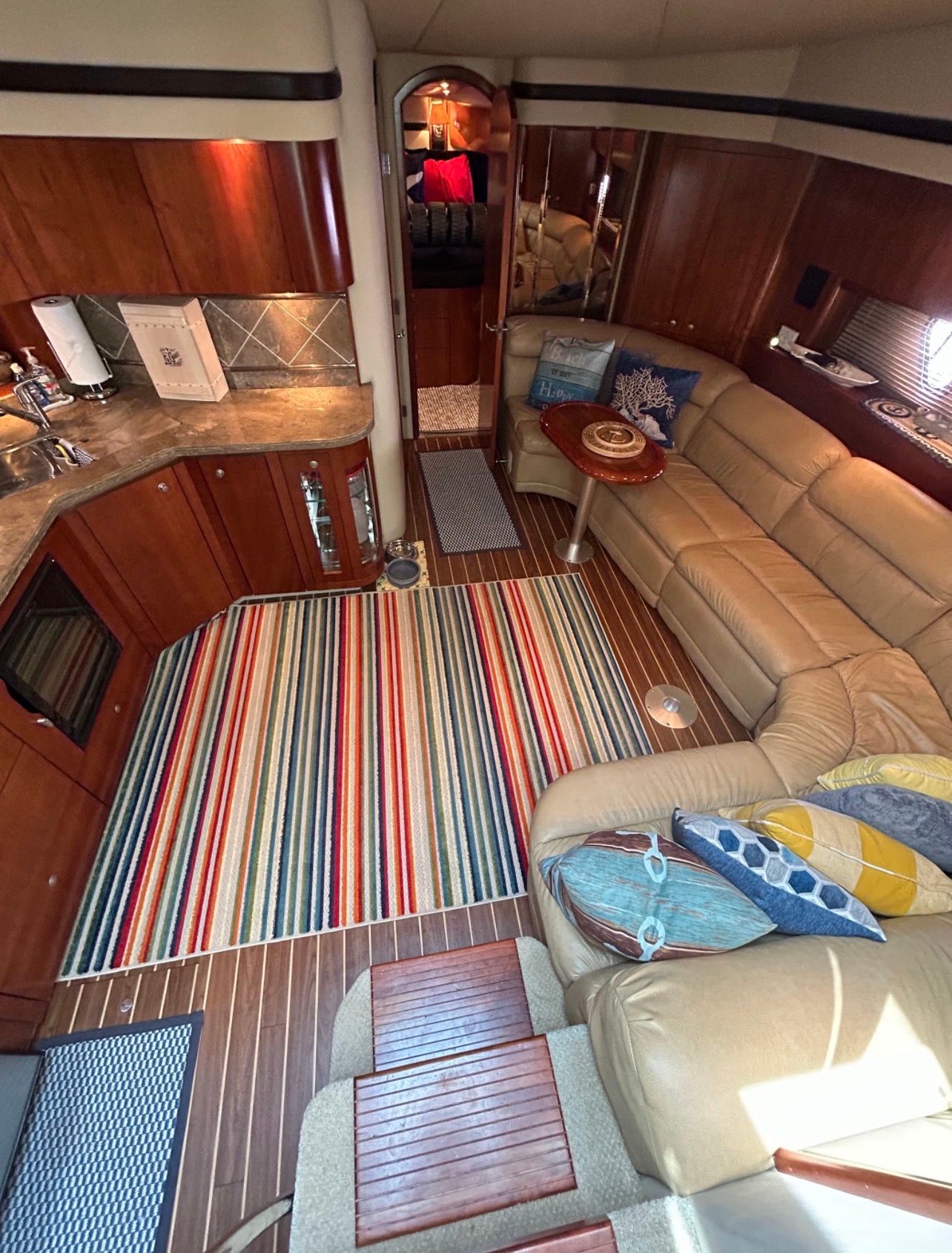 Interior of a luxury yacht with leather sofa, colorful rug, and kitchenette.