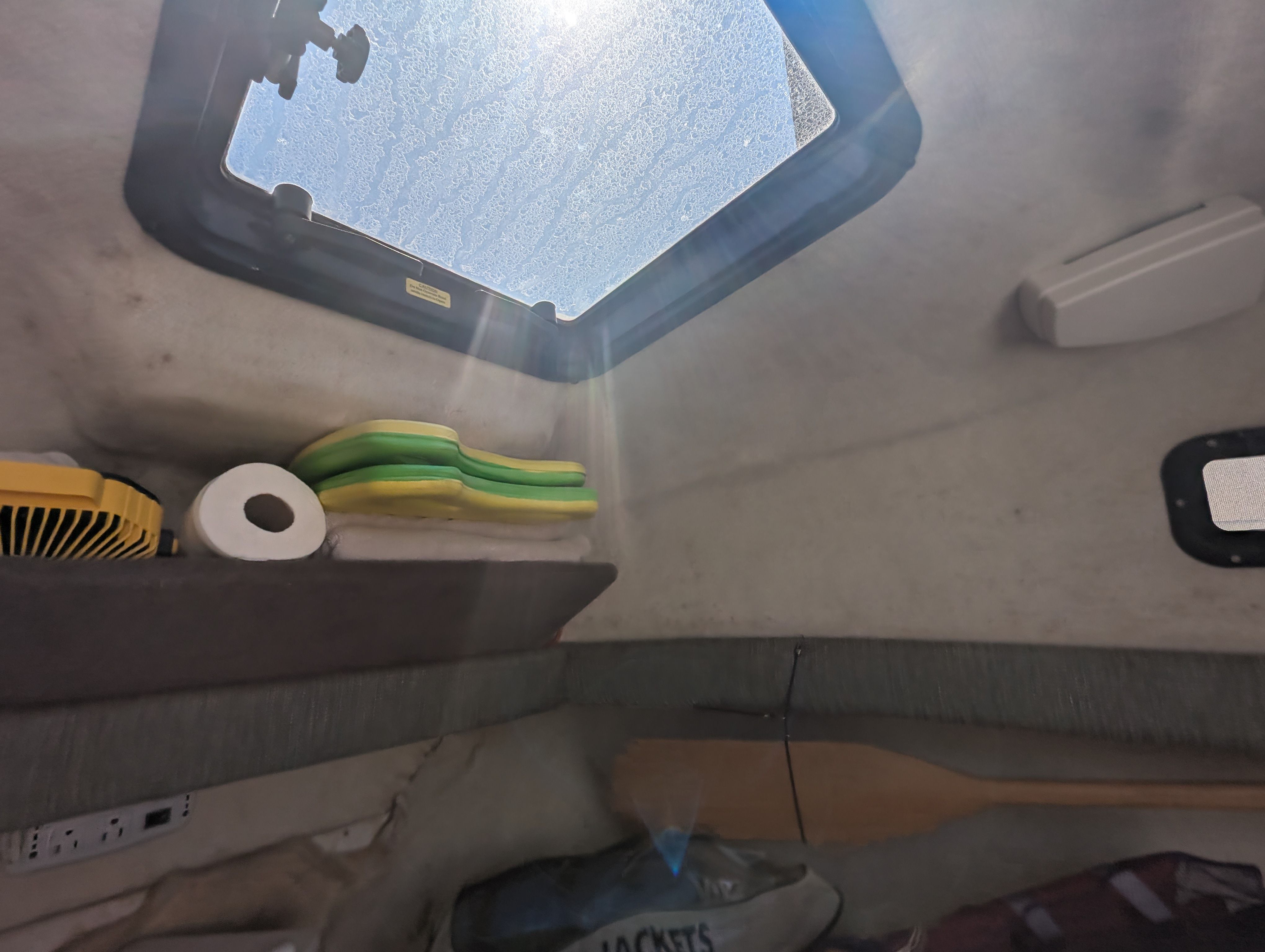 The interior of a boat with a skylight, sponges, and a paddle on the wall.
