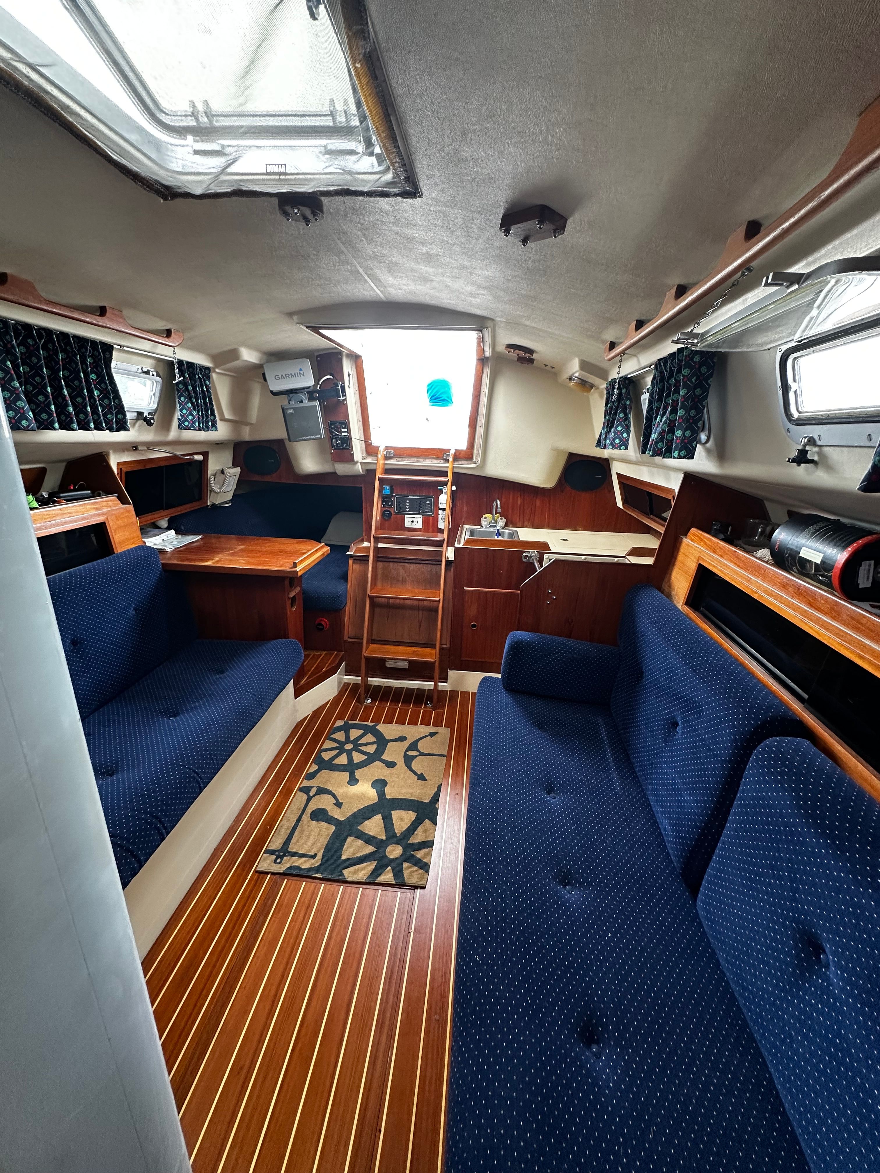 Interior of a 1984 Pearson 303 sailboat with blue upholstery and wooden flooring.
