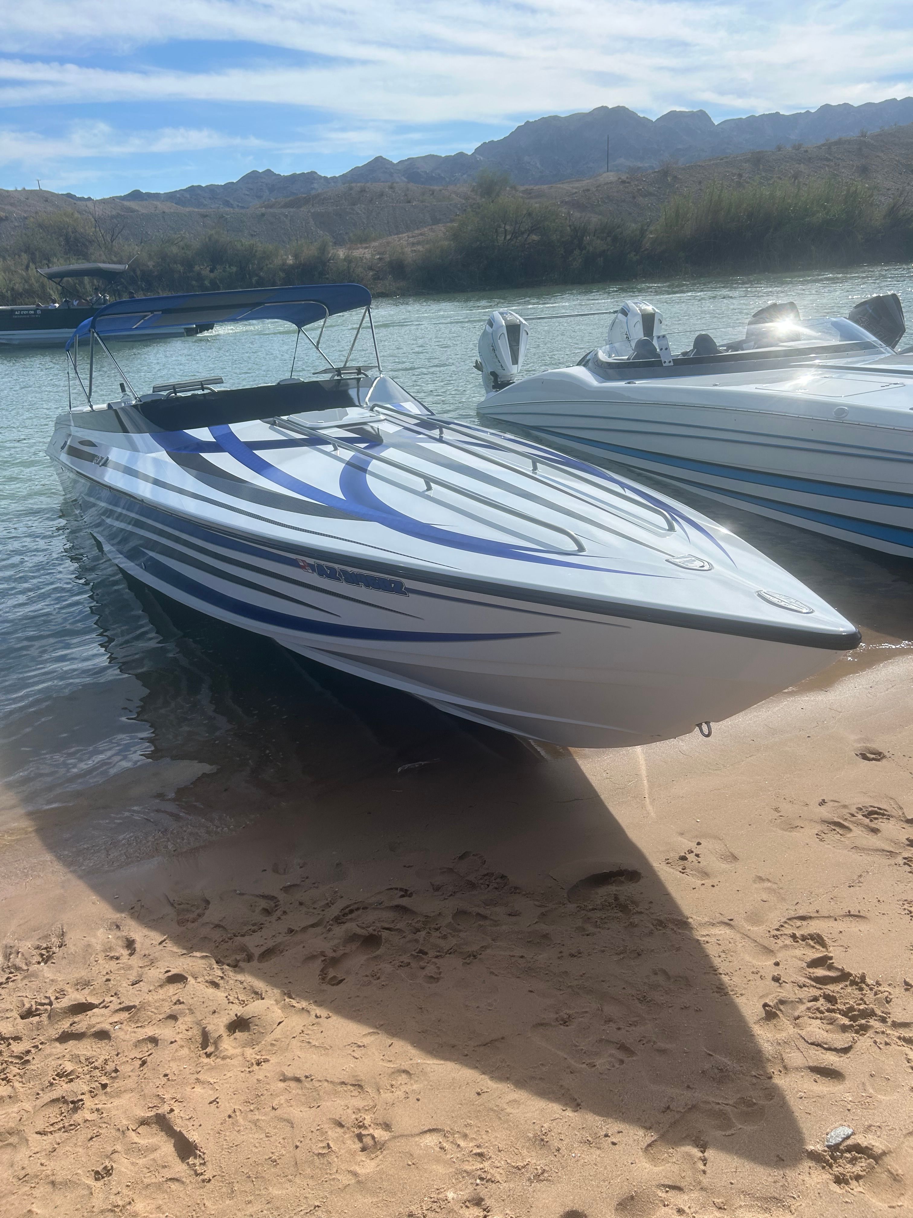A 1999 Lavey Craft 2950 NuEra rests on a sandy shore by calm water.