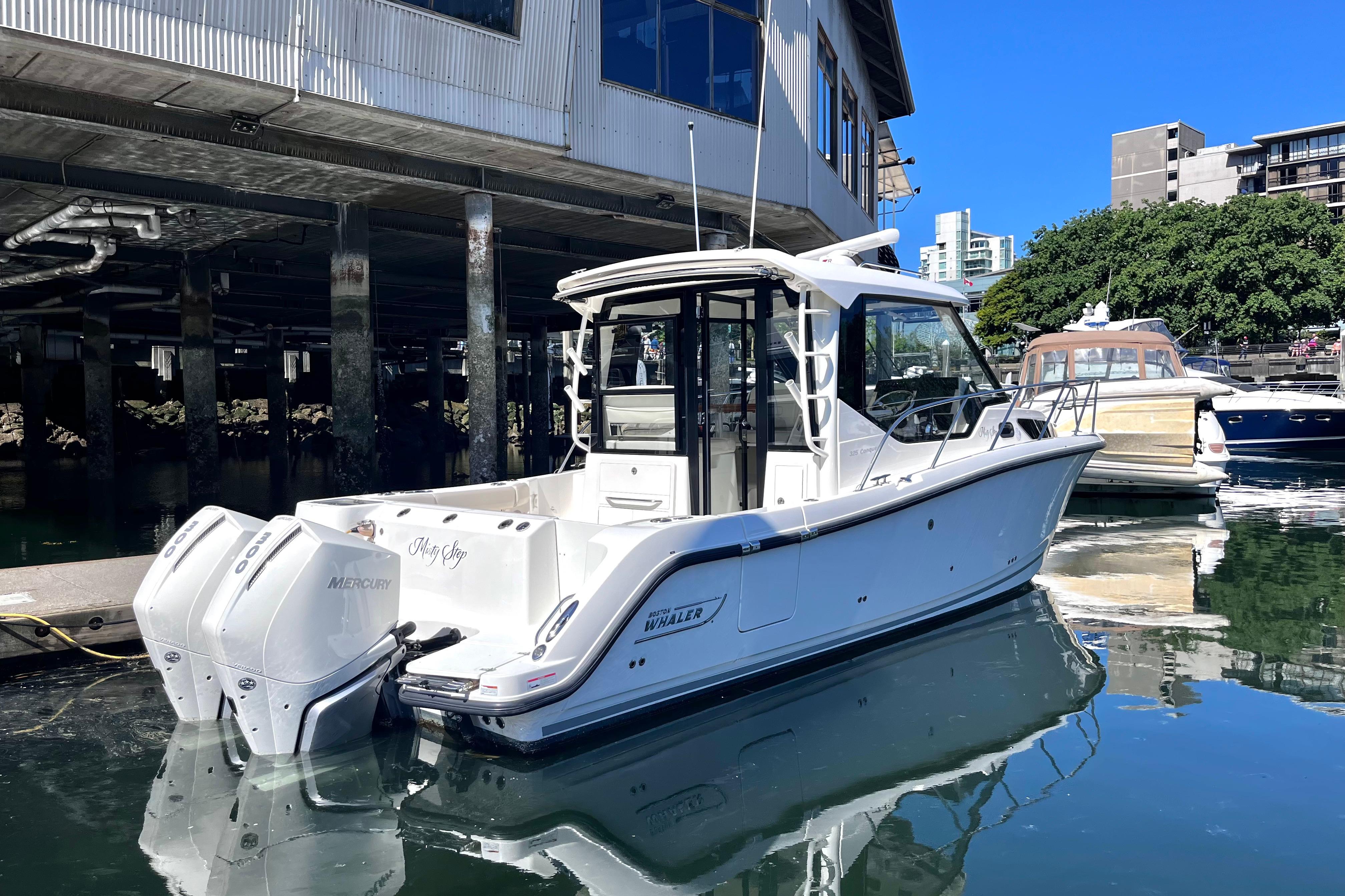 2026 Boston Whaler 325 Conquest Pilothouse docked in a marina, reflecting on calm water.